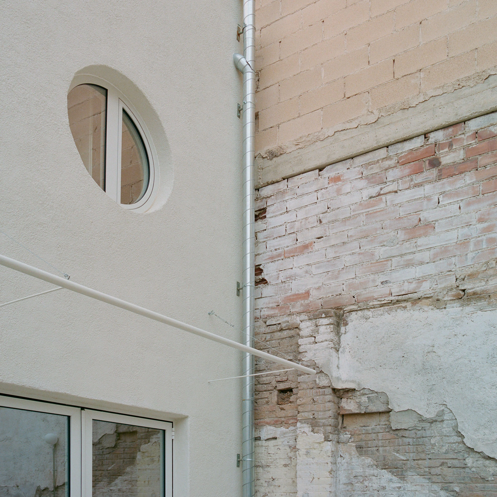 Villa V by Andrea Arriola Fiol and Adrián Mellado Muñoz, photographed by Del Rio Bani — In the rear patio, a round window sits beside the exposed party wall with its old marks and scars
