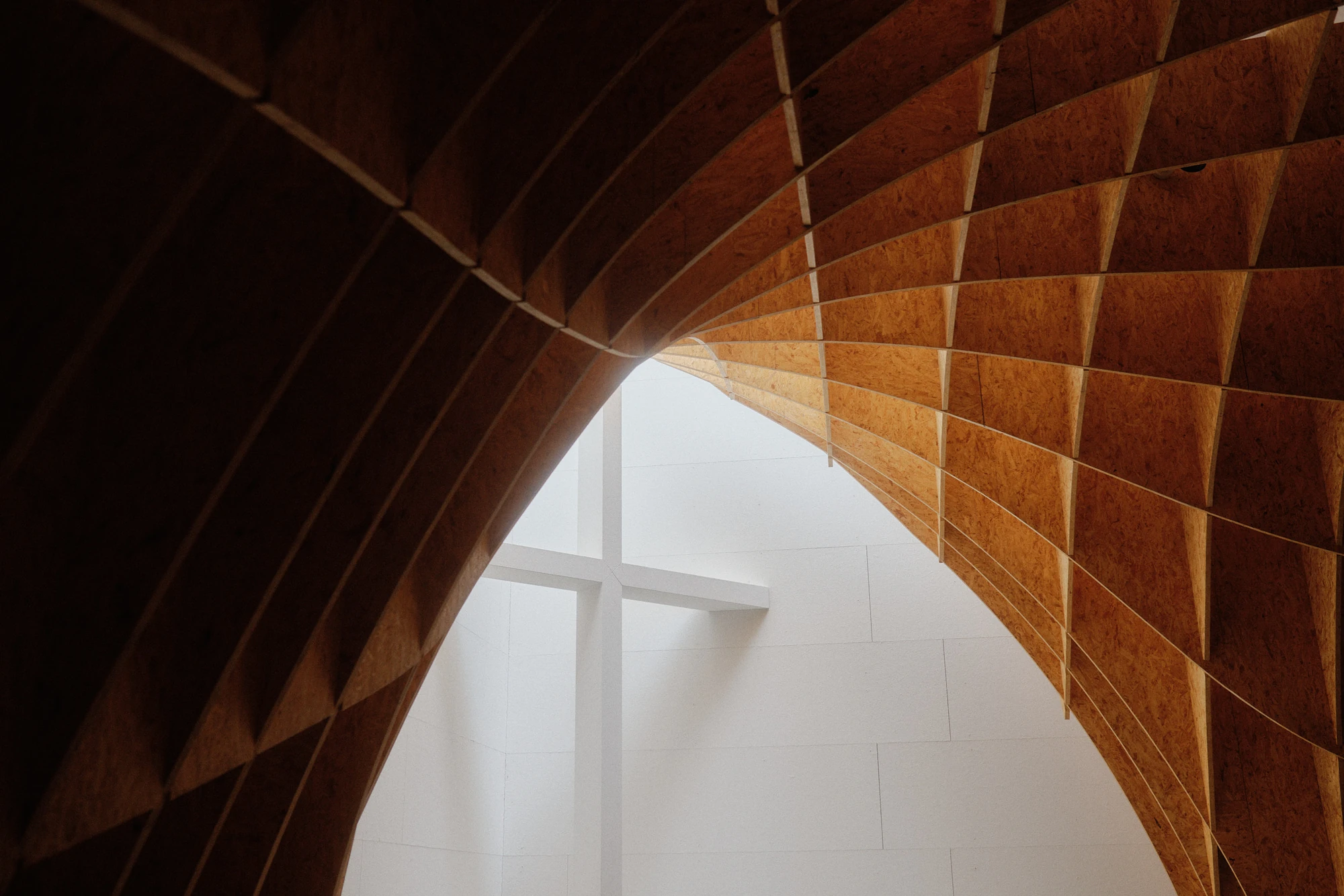 Autobahnkirche Siegerland by schneider+schumacher, photographed by David Altrath — Interior view in which the curving timber vault frames the white altar wall and its cross.