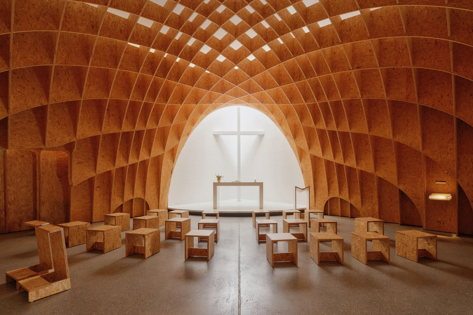 Autobahnkirche Siegerland by schneider+schumacher, photographed by David Altrath — Interior view of the nave from the rear, the timber gridshell vault above rows of low stools facing the white altar.