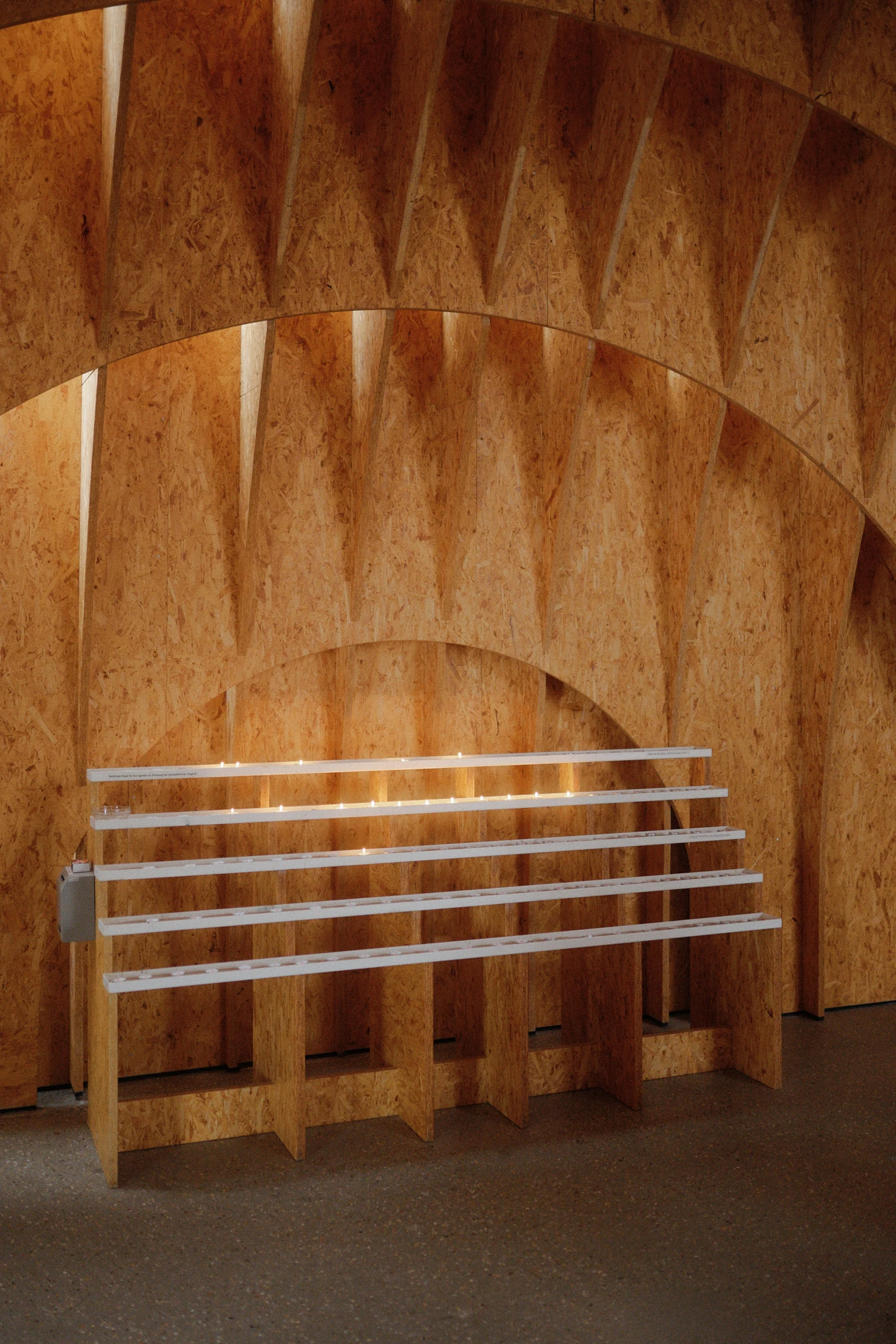 Autobahnkirche Siegerland by schneider+schumacher, photographed by David Altrath — Interior view of a white candle rack holding lit candles against the curving timber wall.