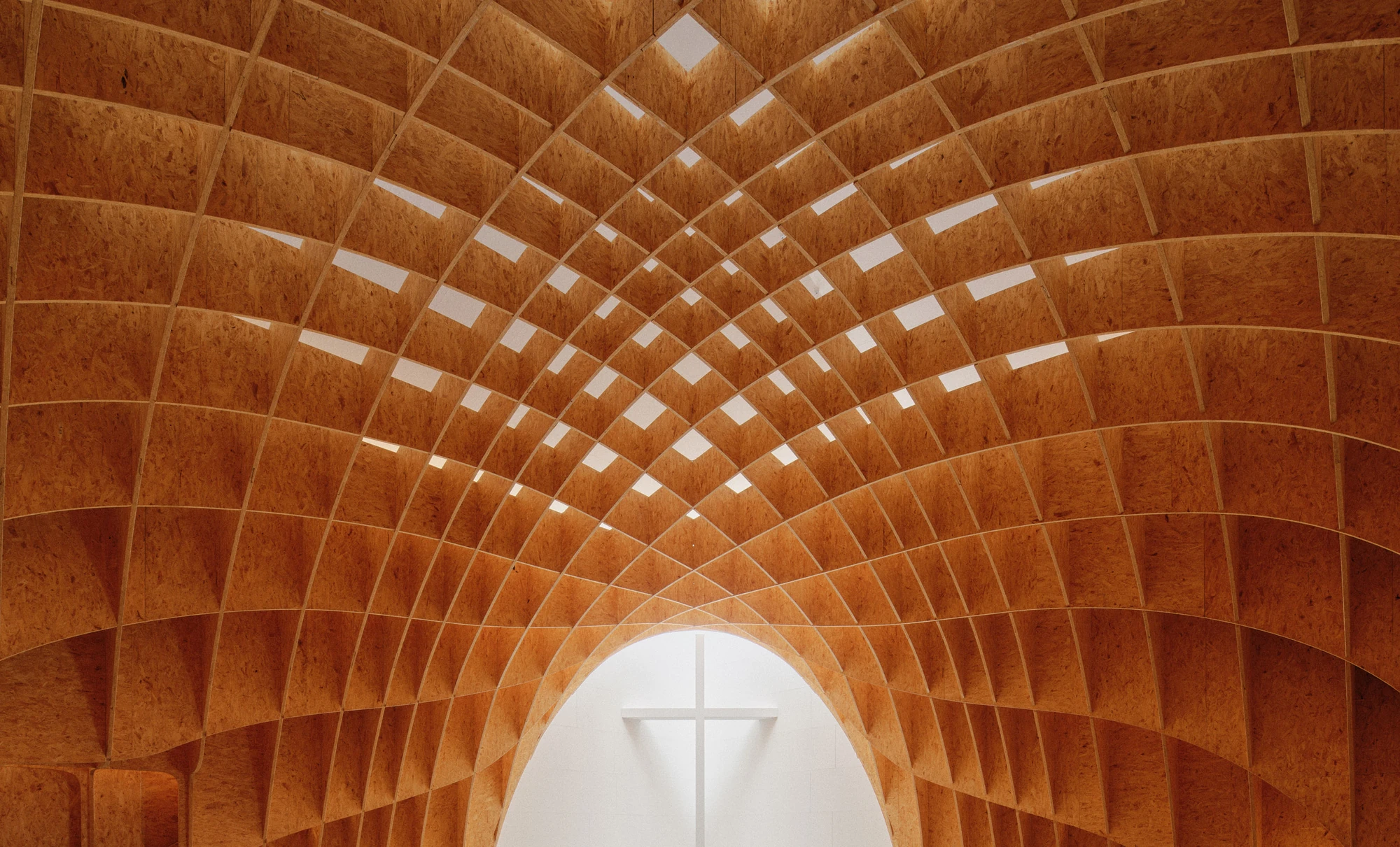 Autobahnkirche Siegerland by schneider+schumacher, photographed by David Altrath — Interior view looking up into the timber gridshell with its strip skylights, the altar cross glimpsed through the arch below.
