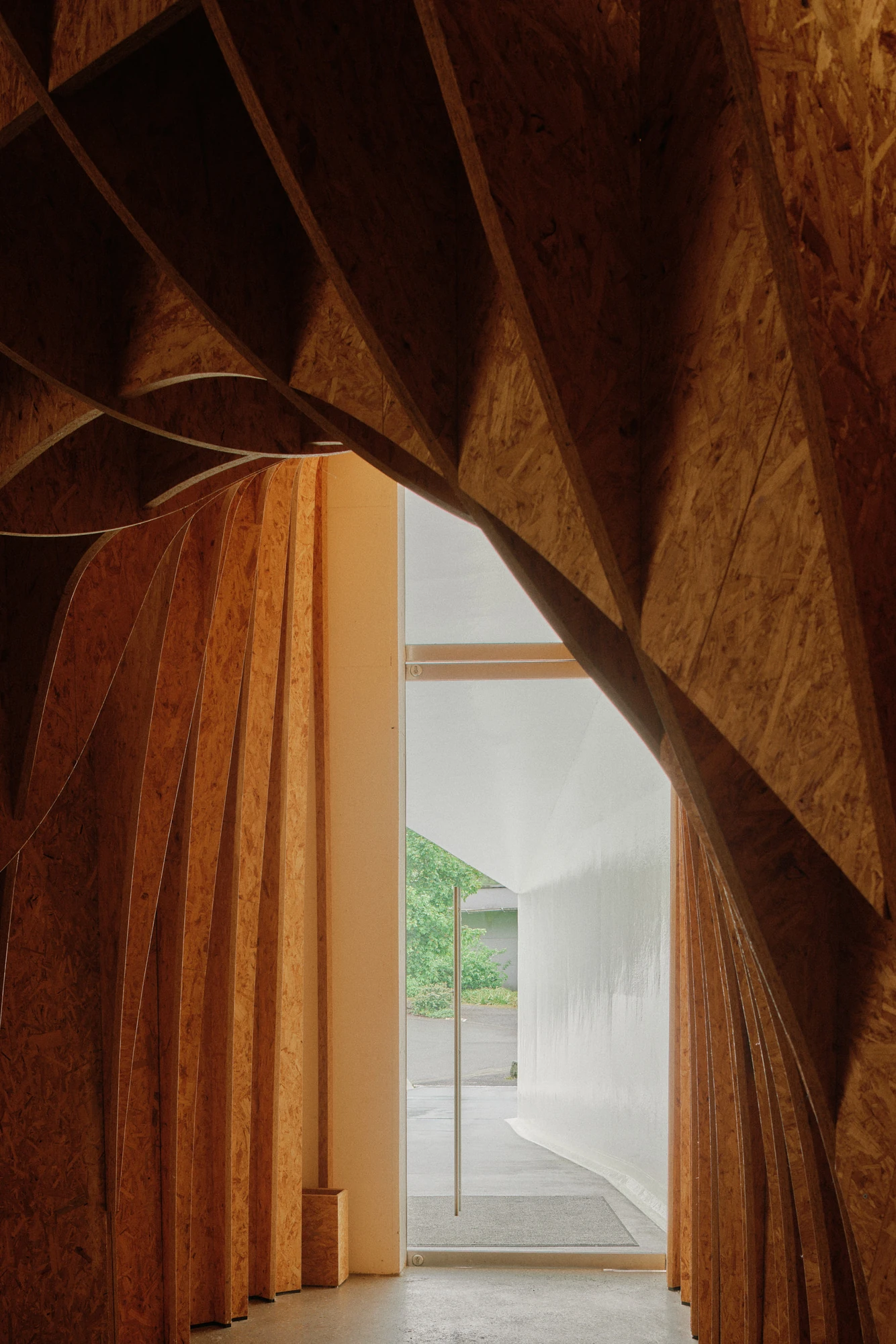 Autobahnkirche Siegerland by schneider+schumacher, photographed by David Altrath — Interior view through the fanning timber ribs toward the glazed entrance and the daylight beyond.