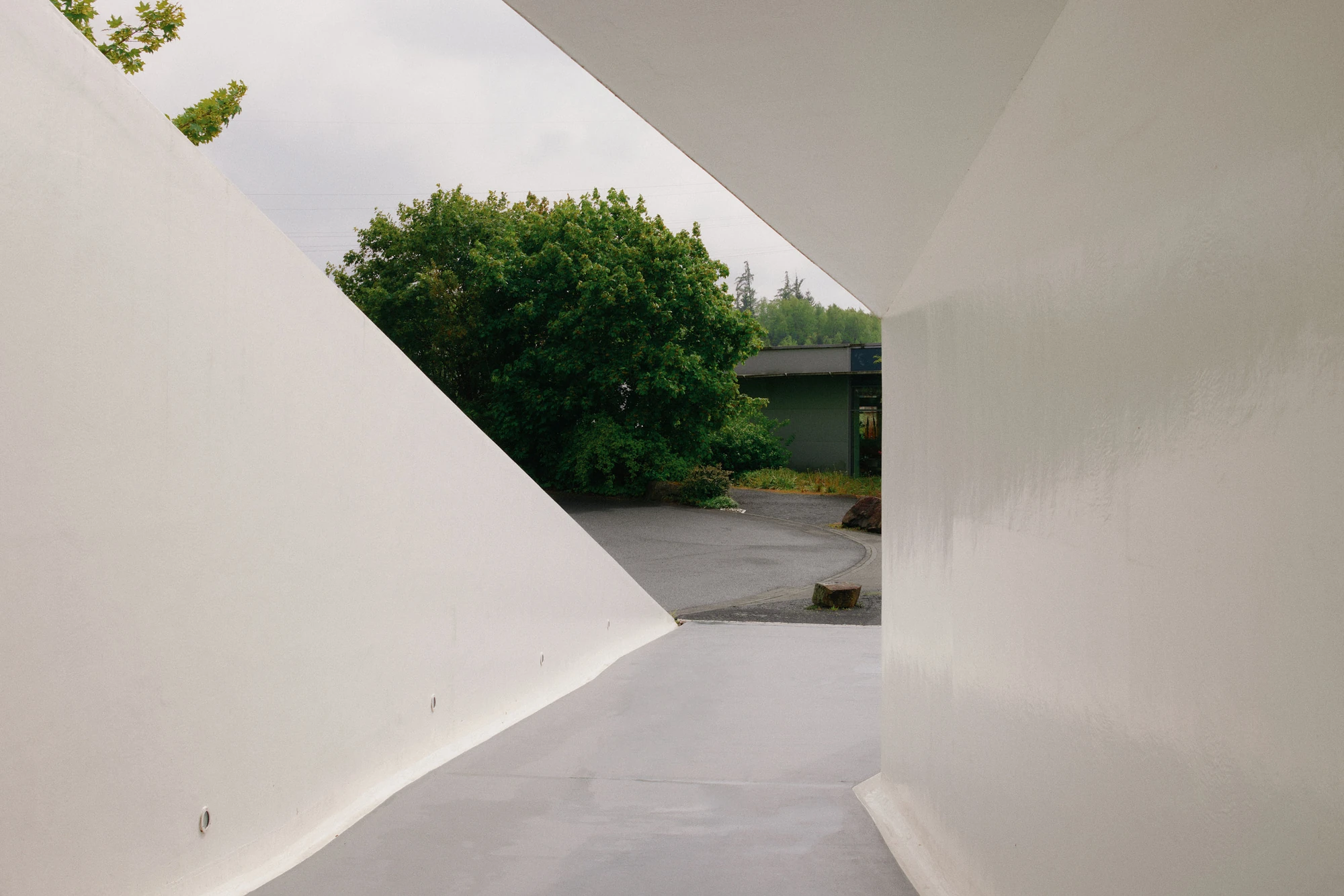 Autobahnkirche Siegerland by schneider+schumacher, photographed by David Altrath — Exterior view of the white entrance approached along a sloping walkway between canted walls.