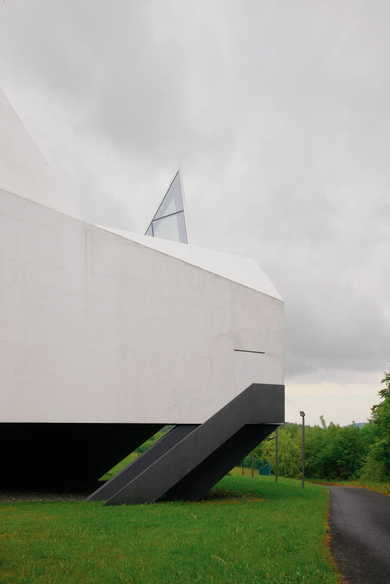 Autobahnkirche Siegerland by schneider+schumacher, photographed by David Altrath — Exterior view of the side wall with the black steel access stair descending and a spire tip above.