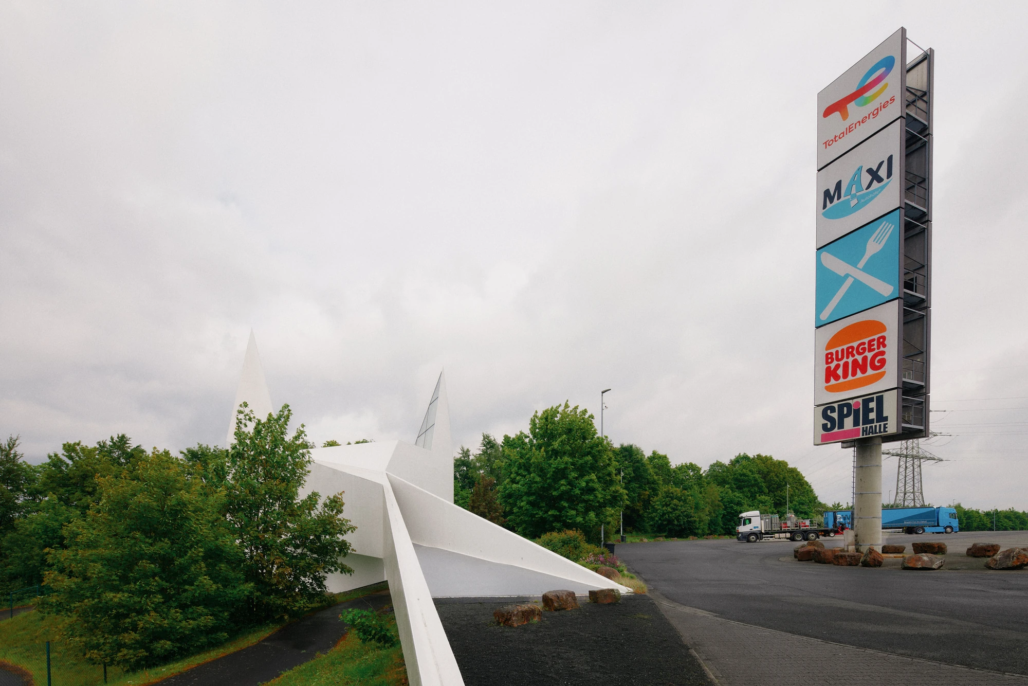 Autobahnkirche Siegerland by schneider+schumacher, photographed by David Altrath — Exterior view of the two-spired church standing beside the service area and its tall illuminated sign tower.