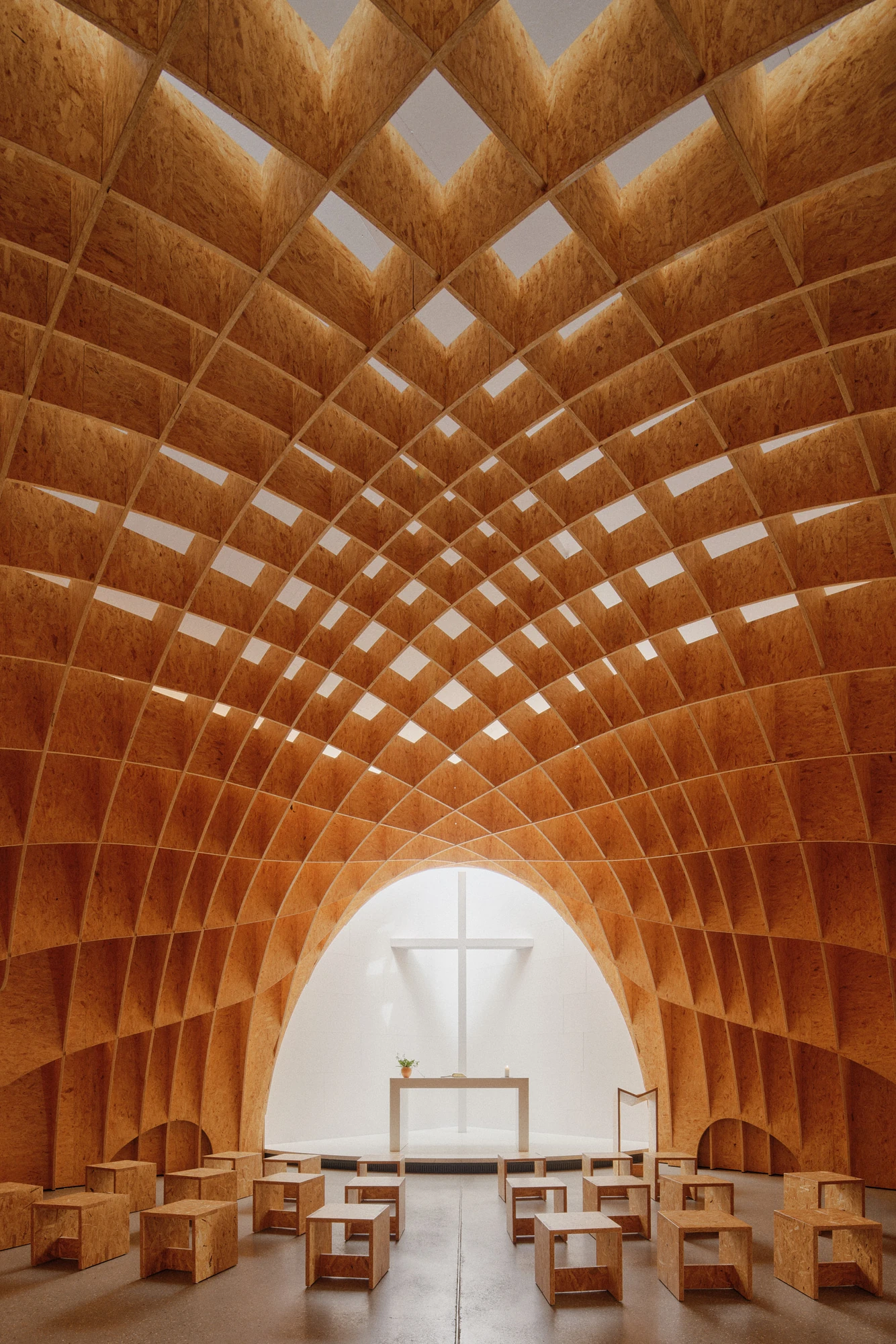 Autobahnkirche Siegerland by schneider+schumacher, photographed by David Altrath — Interior view toward the white apse with its cross and altar beneath the timber gridshell vault.