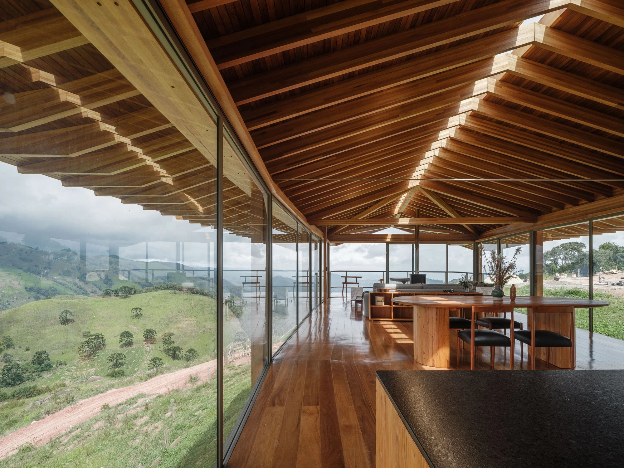 Casa Fazenda Bocaina by Arquipélago Arquitetos + Mariana Caires, photographed by Pedro Kok — The open living and dining space running along the glazed wall beneath the pitched timber roof.