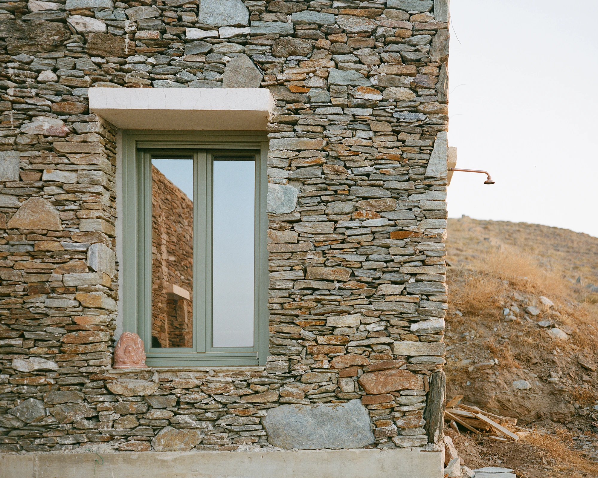 House Thermia by RAUM, photographed by Benoit Chailleux — The house against an open sky, seen from across the hillside at Thermia.