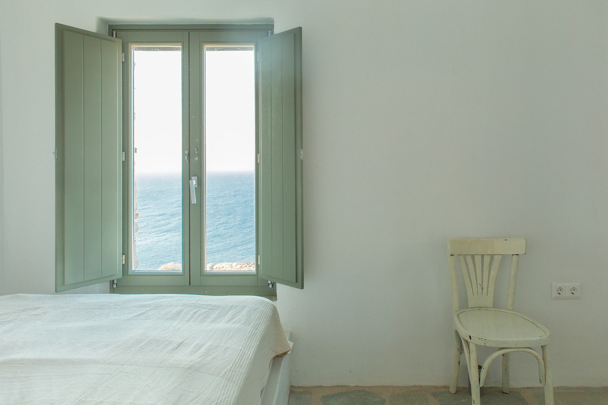 House Thermia by RAUM, photographed by Benoit Chailleux — A bedroom with its window open to the sea at Thermia.