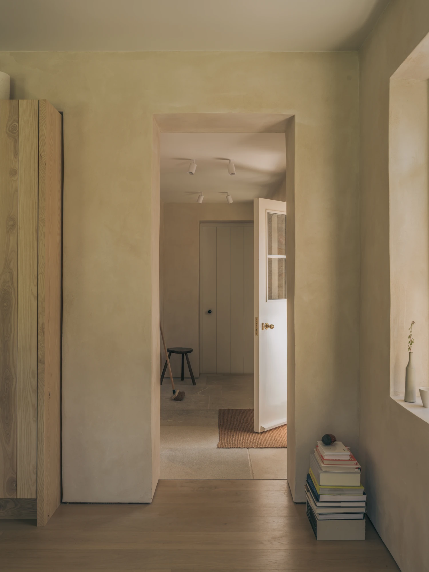 Cairngorm Cottage by Architecture Office, photographed by Richard Gaston — A view through a doorway into the hall beyond, clay-plaster walls and a tall ash cupboard to one side.