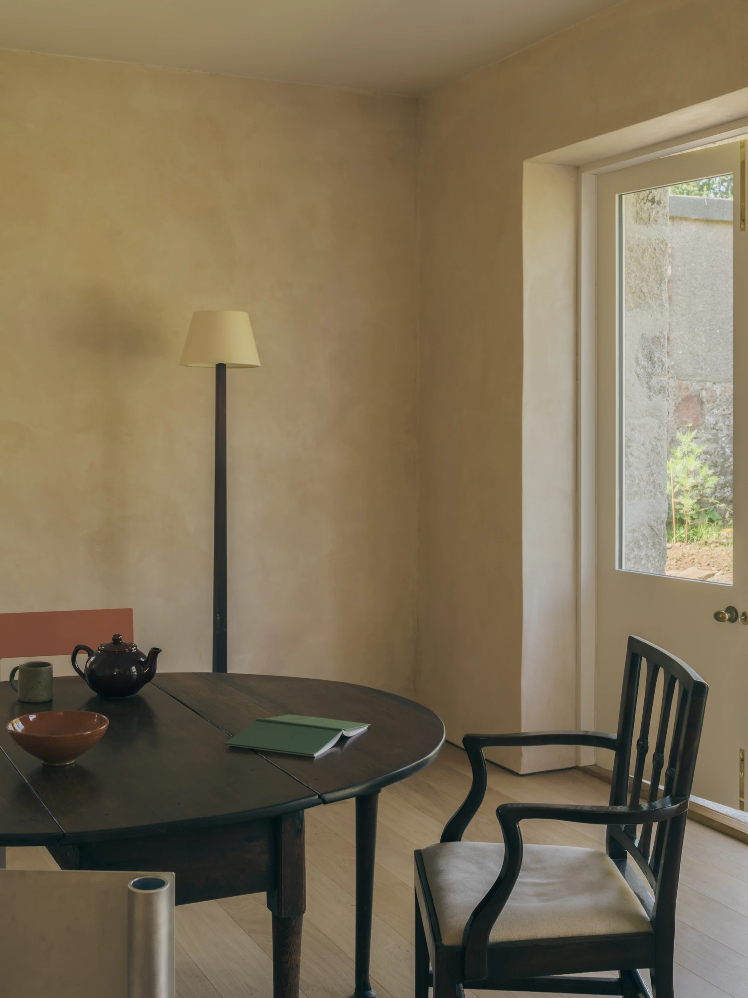 Cairngorm Cottage by Architecture Office, photographed by Richard Gaston — A corner of the dining room where a glazed door opens to the garden through a deep-set opening in the masonry.