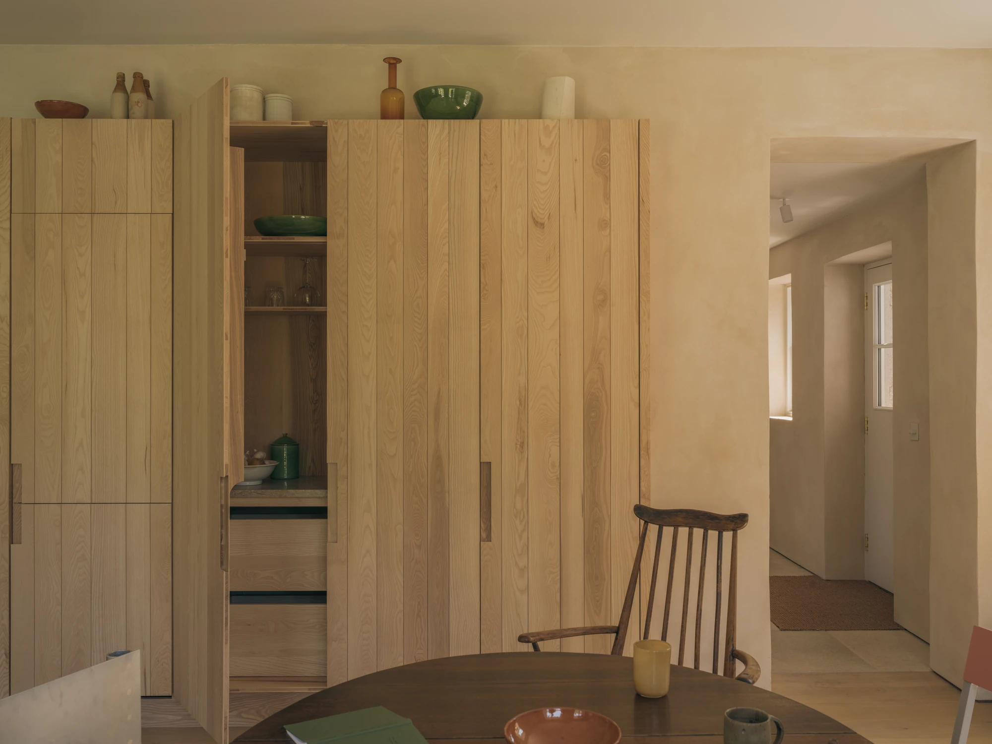 Cairngorm Cottage by Architecture Office, photographed by Richard Gaston — The ash larder opened to its shelves, with the dining table in front and a passage leading back through the house.