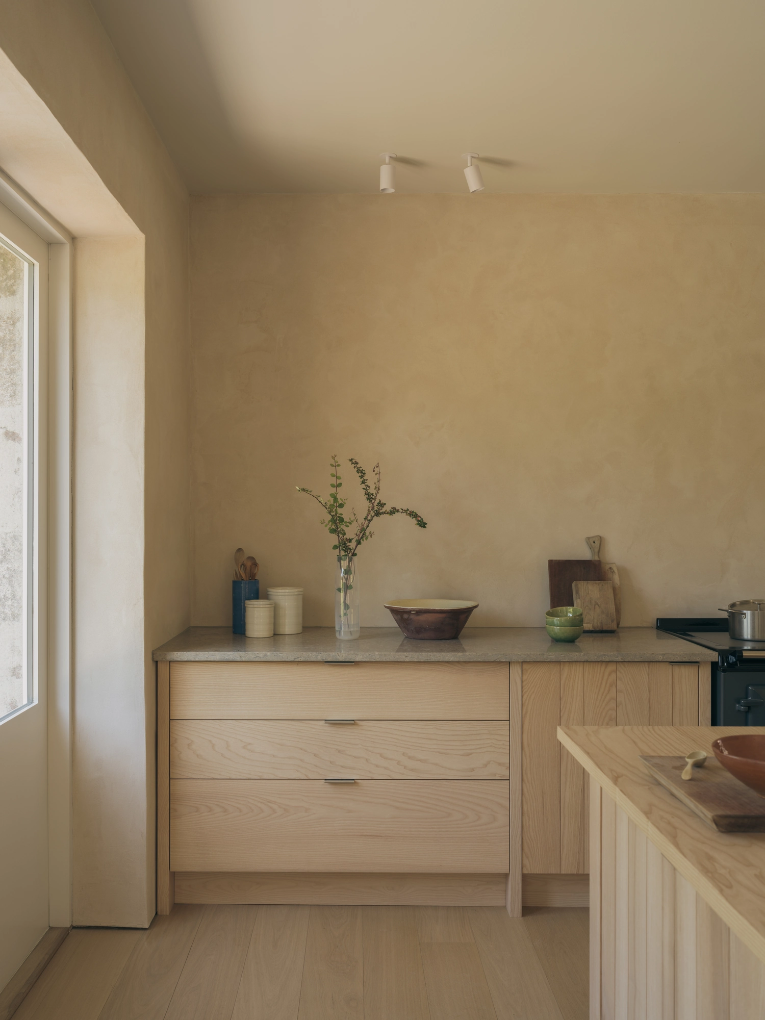 Cairngorm Cottage by Architecture Office, photographed by Richard Gaston — A run of Scottish ash drawers below a stone worktop, next to a window set deep in the clay-plaster wall.