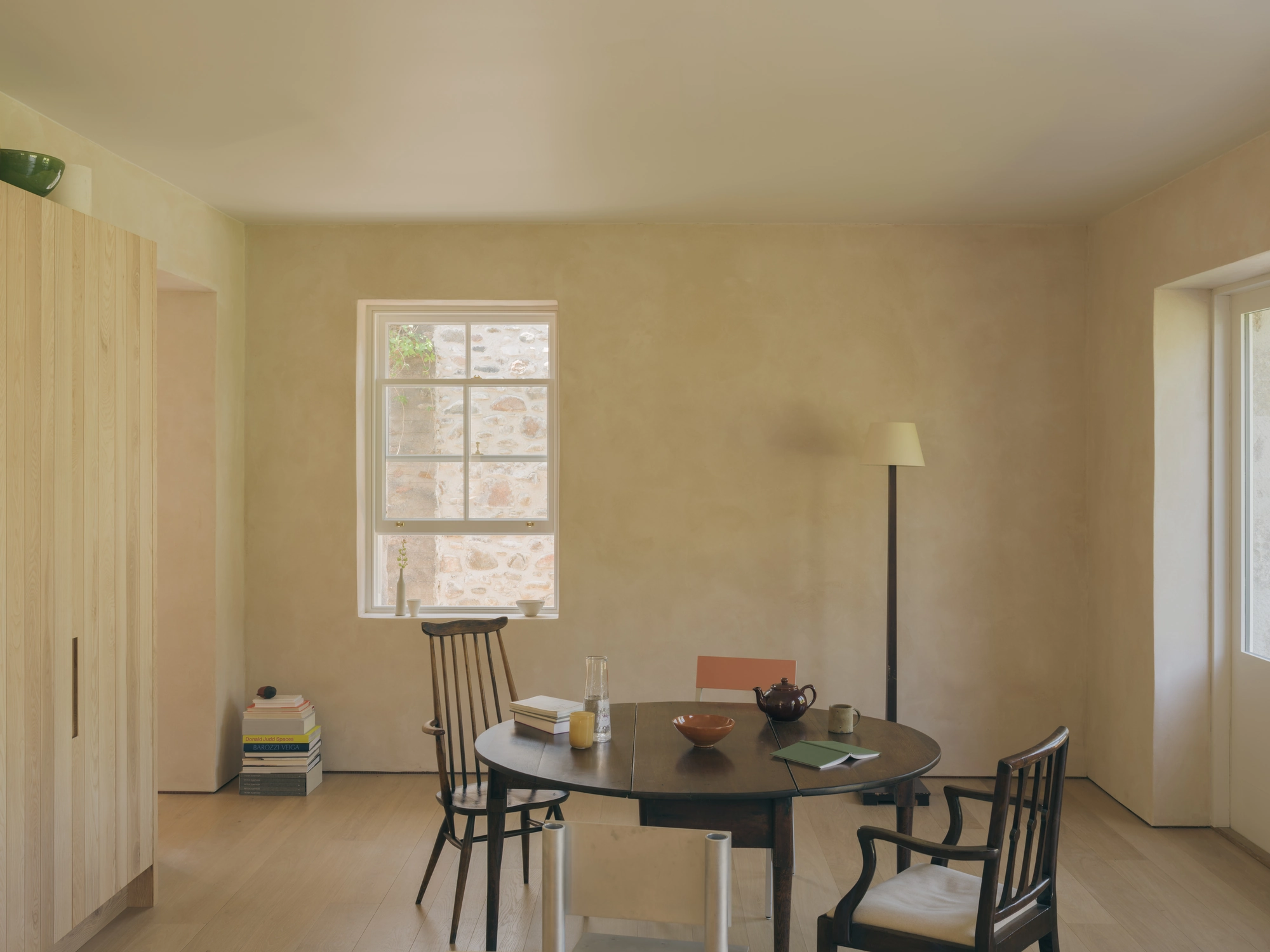 Cairngorm Cottage by Architecture Office, photographed by Richard Gaston — The dining room under clay plaster, a round table set below a window in the far wall.