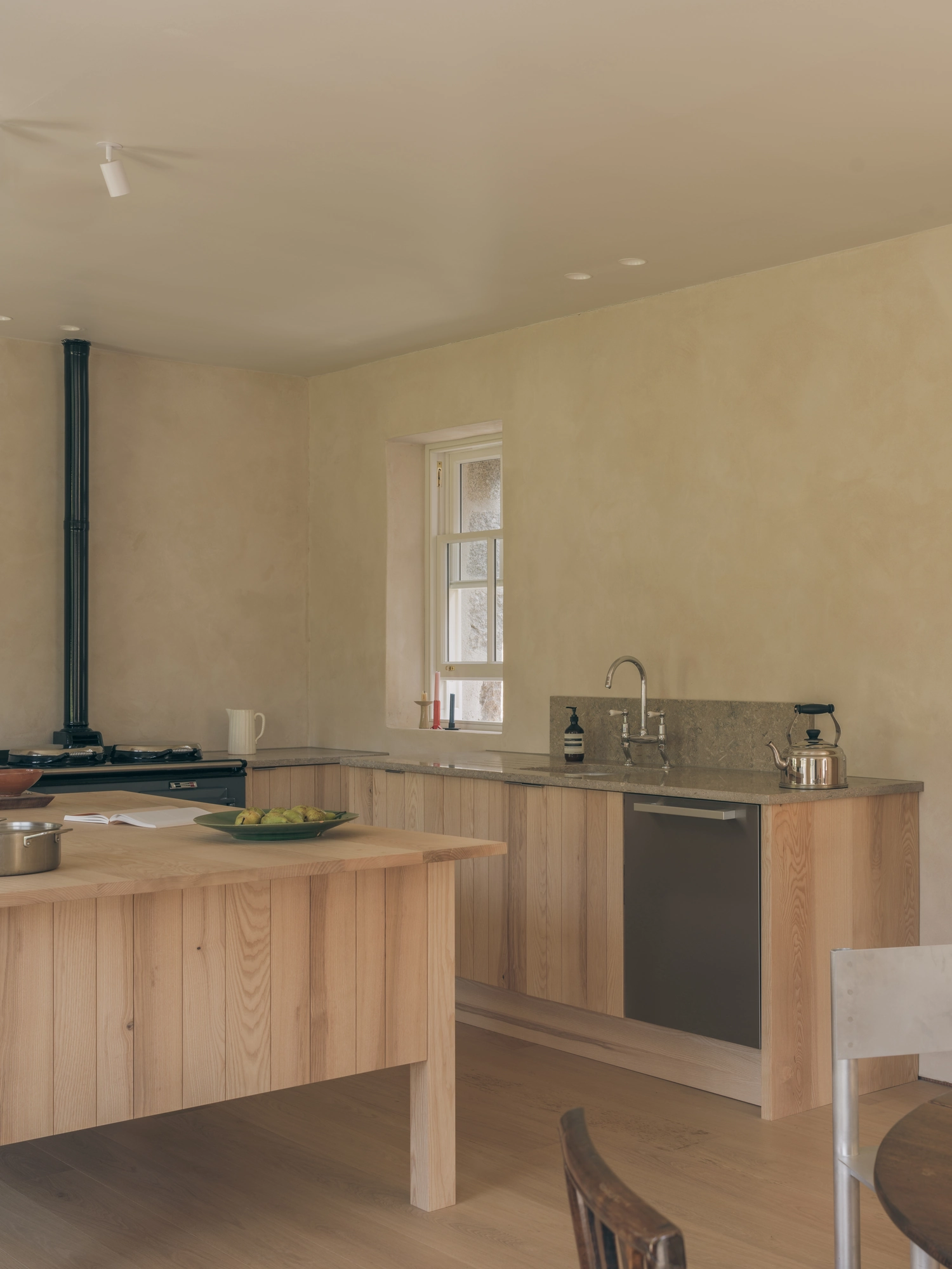 Cairngorm Cottage by Architecture Office, photographed by Richard Gaston — The kitchen sink and stone worktop under a deep-set window, the central island to the left.