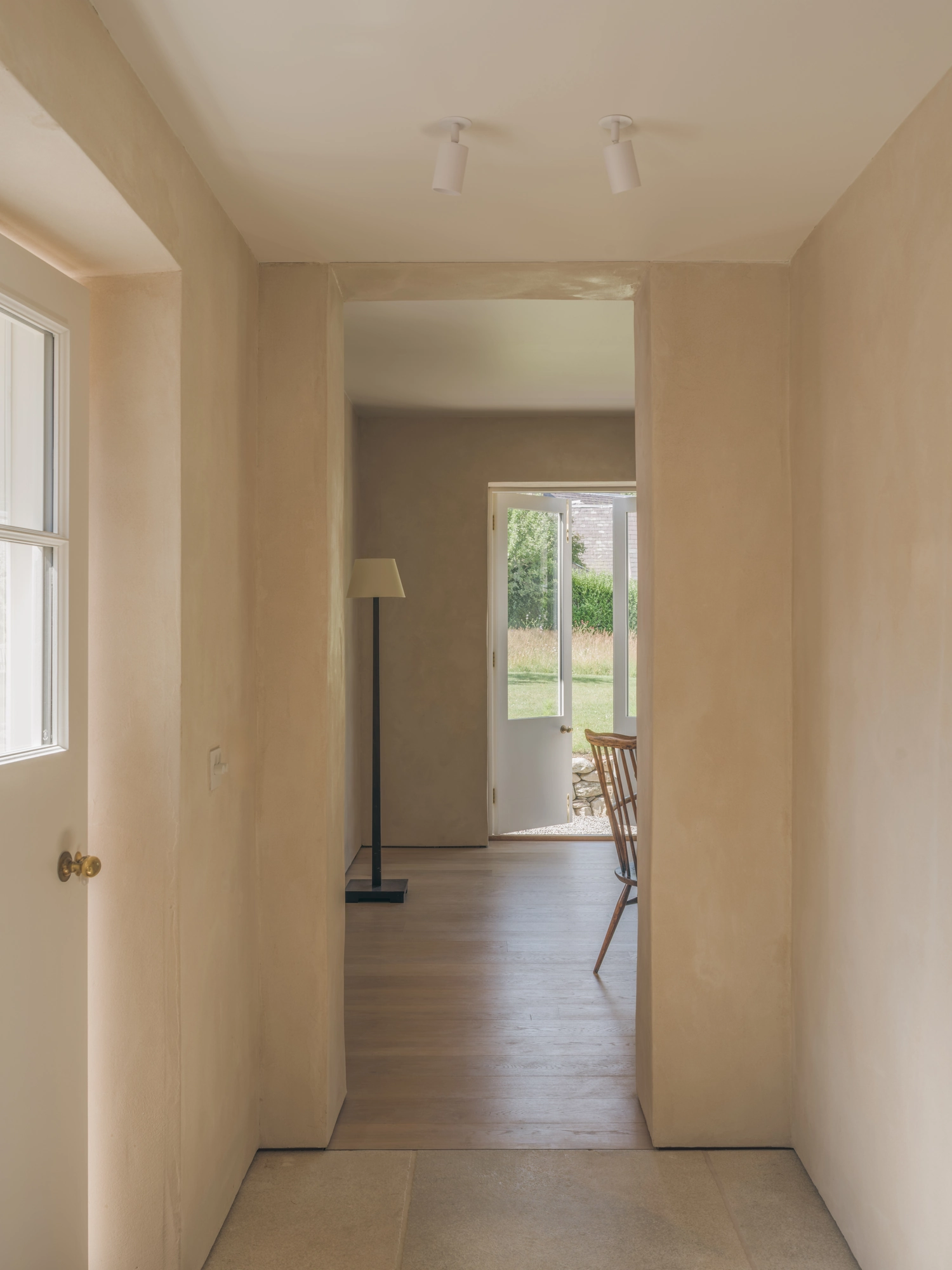 Cairngorm Cottage by Architecture Office, photographed by Richard Gaston — A hallway through the house to a glazed door open to the garden, clay-plaster walls on either side.