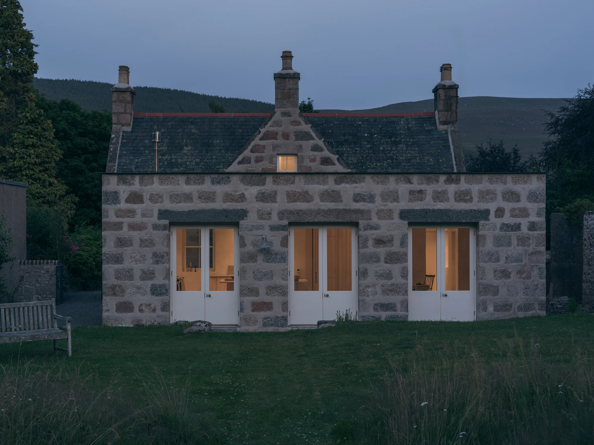 Cairngorm Cottage by Architecture Office, photographed by Richard Gaston — The extension at dusk, the three sets of glazed doors lit from within.