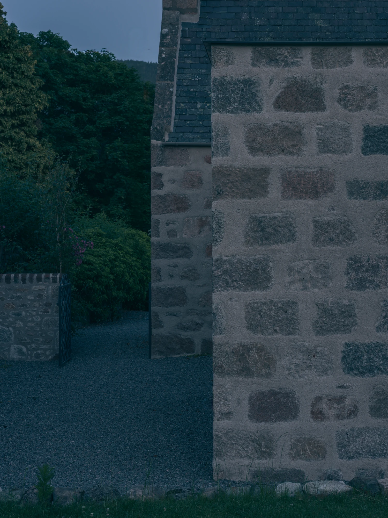 Cairngorm Cottage by Architecture Office, photographed by Richard Gaston — A granite corner at dusk beside a low stone boundary wall.