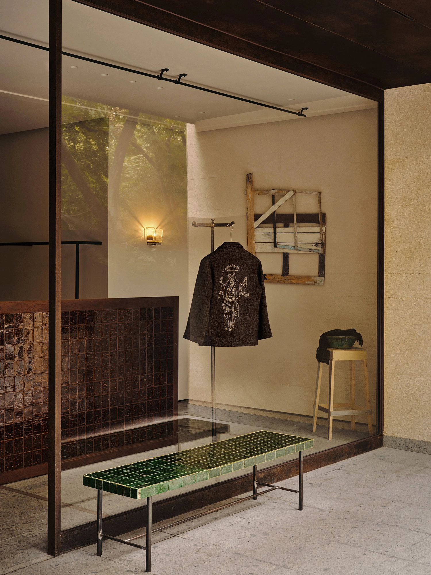 Conceived by Cotemp by ONOAA STUDIO, photographed by Jonathan Leijonhufvud — A jacket on a rail seen through the shopfront glass, with a stool and a low bench.