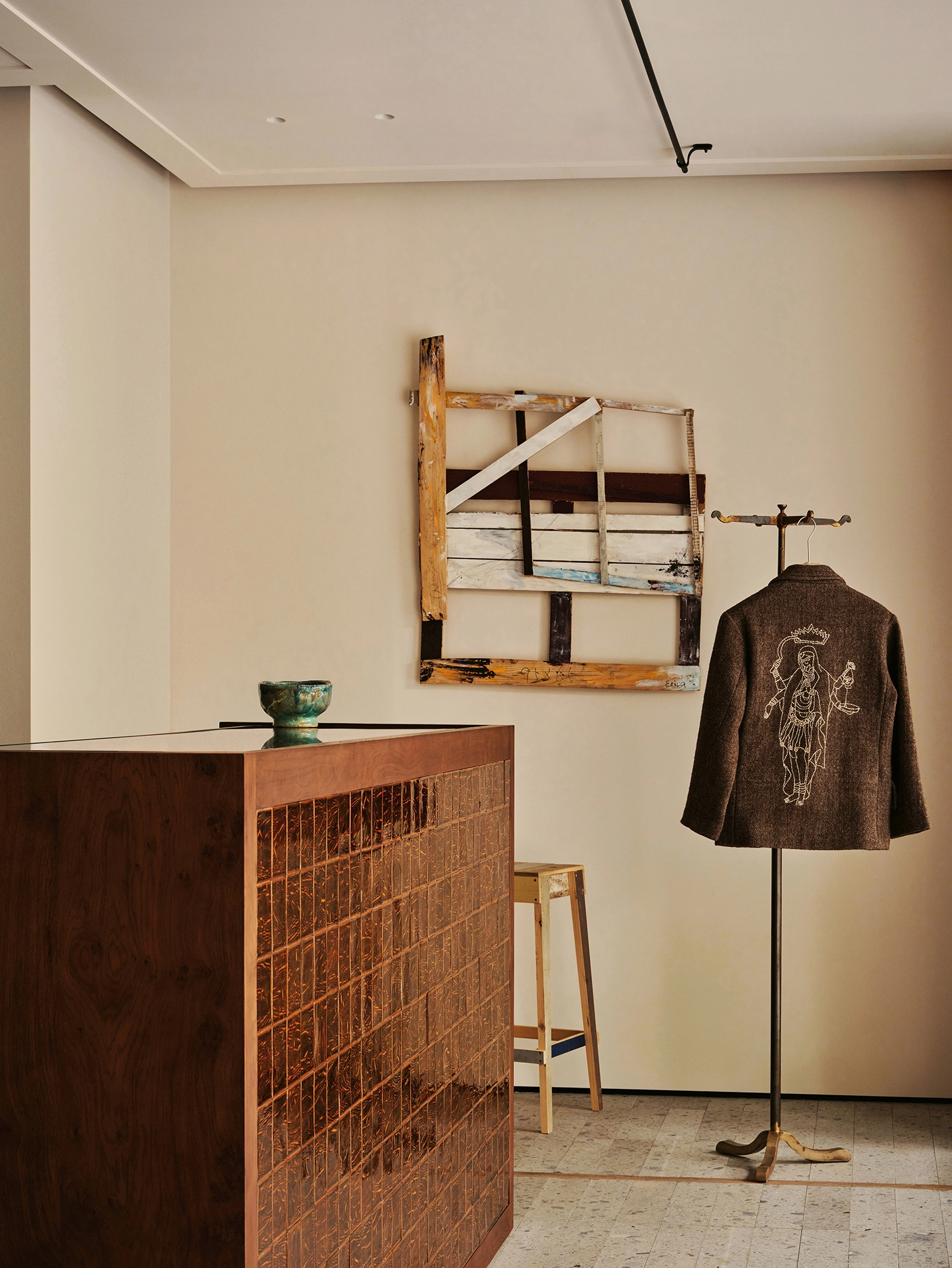 Conceived by Cotemp by ONOAA STUDIO, photographed by Jonathan Leijonhufvud — A jacket on a standing rail beside a display counter, with a stool and a panel on the wall.