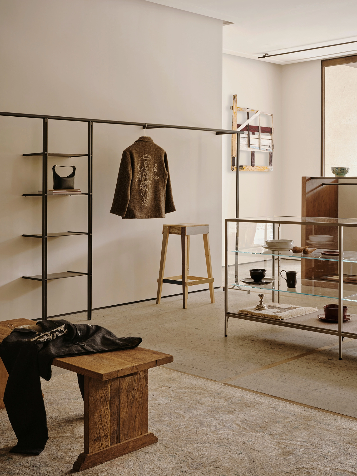 Conceived by Cotemp by ONOAA STUDIO, photographed by Jonathan Leijonhufvud — A wide view of the ground floor with wall shelving, a jacket on a rail, a display case and a bench.