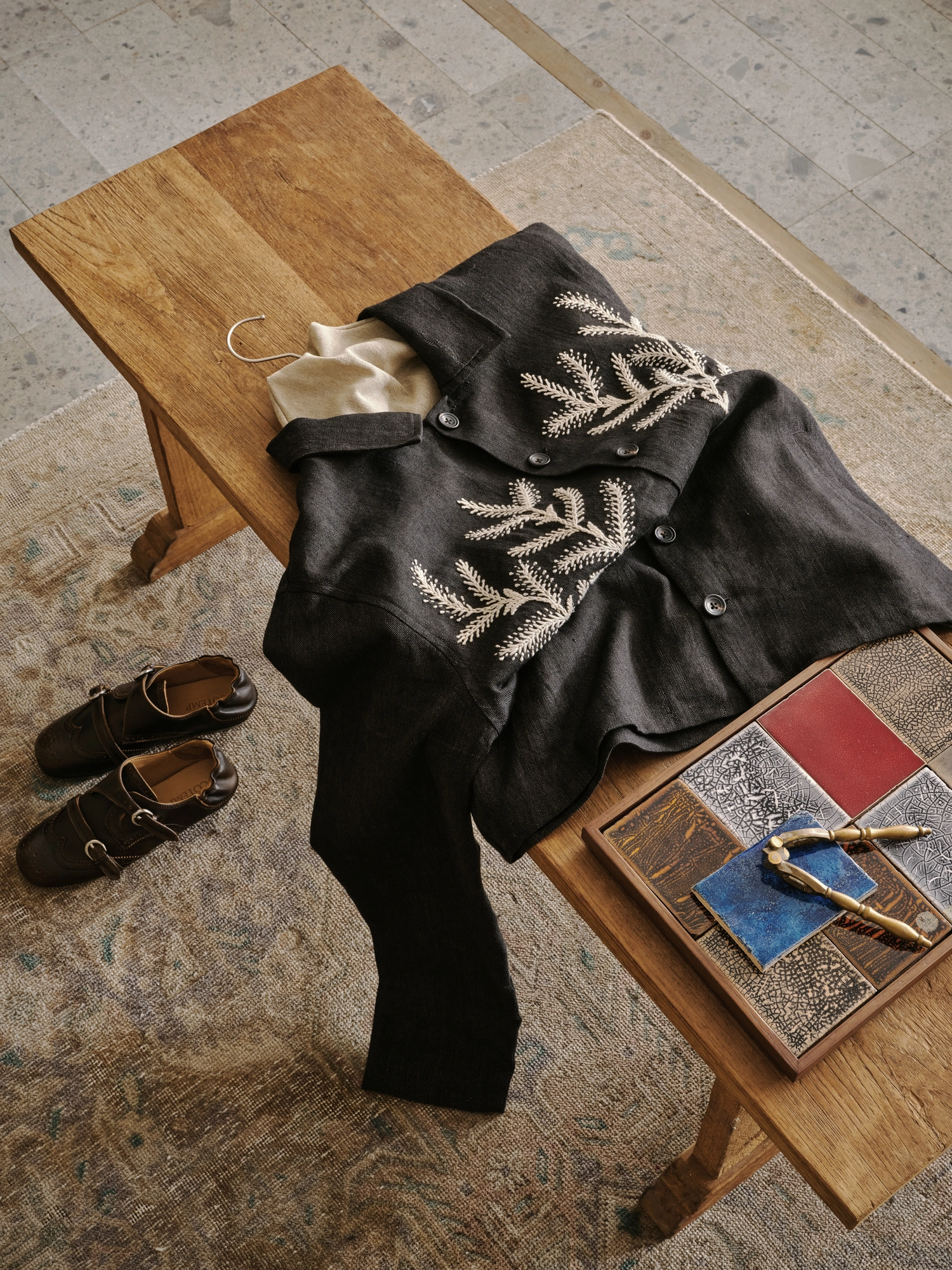 Conceived by Cotemp by ONOAA STUDIO, photographed by Jonathan Leijonhufvud — A garment laid across a bench, a pair of shoes on the floor, and a tray of samples alongside.