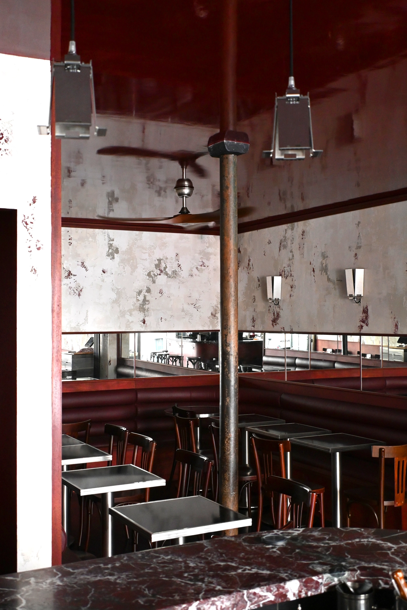 WINONA by Romain Basile Petrot, photographed by Romain Roucoules, Carla Beaujardin — A wider view down the room to the banquette at the back, the deep red marble counter in the foreground and the custom lights by Petrot overhead.