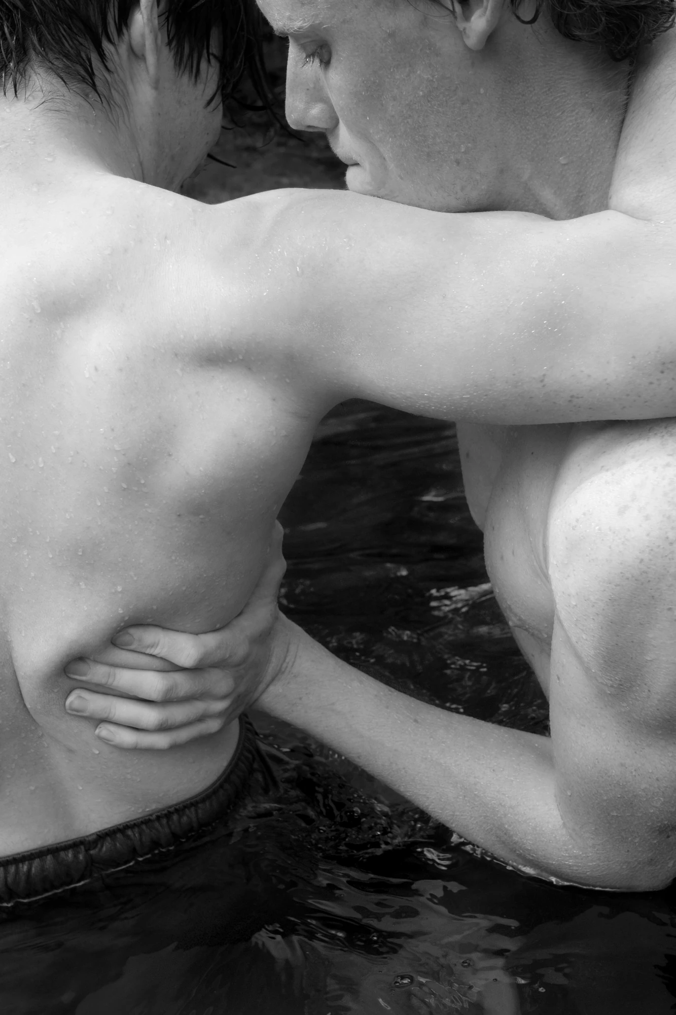 Down by the Hudson by Caleb Stein, photographed by Caleb Stein — Bode & Owen, Wrestling (2022), two young men locked arm around back and chest in the dark water