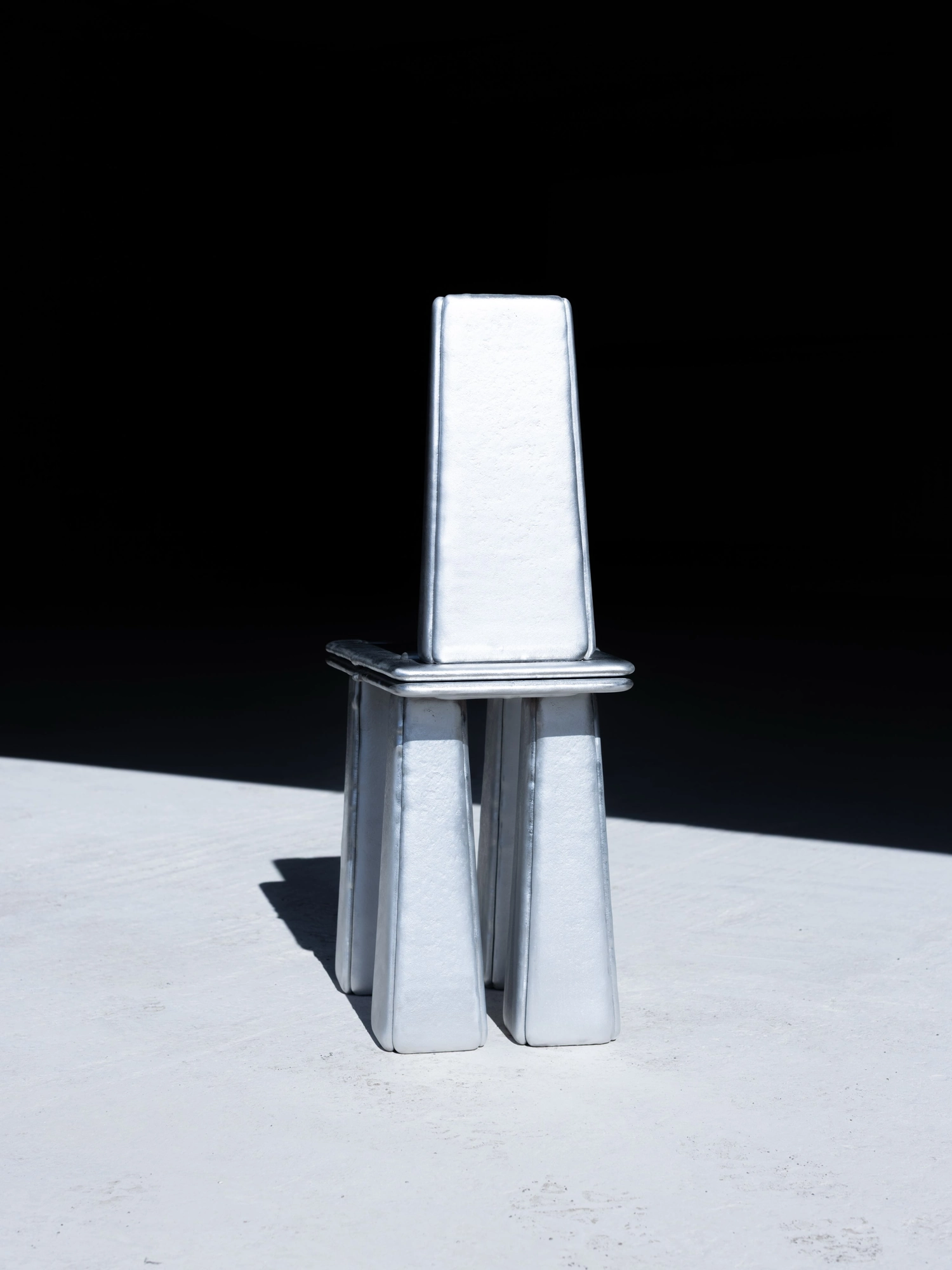 Ingot by Marc Sweeney, photographed by Marc Sweeney — Front elevation of the cast aluminium chair, the tall tapered back above four legs that open to a central gap.