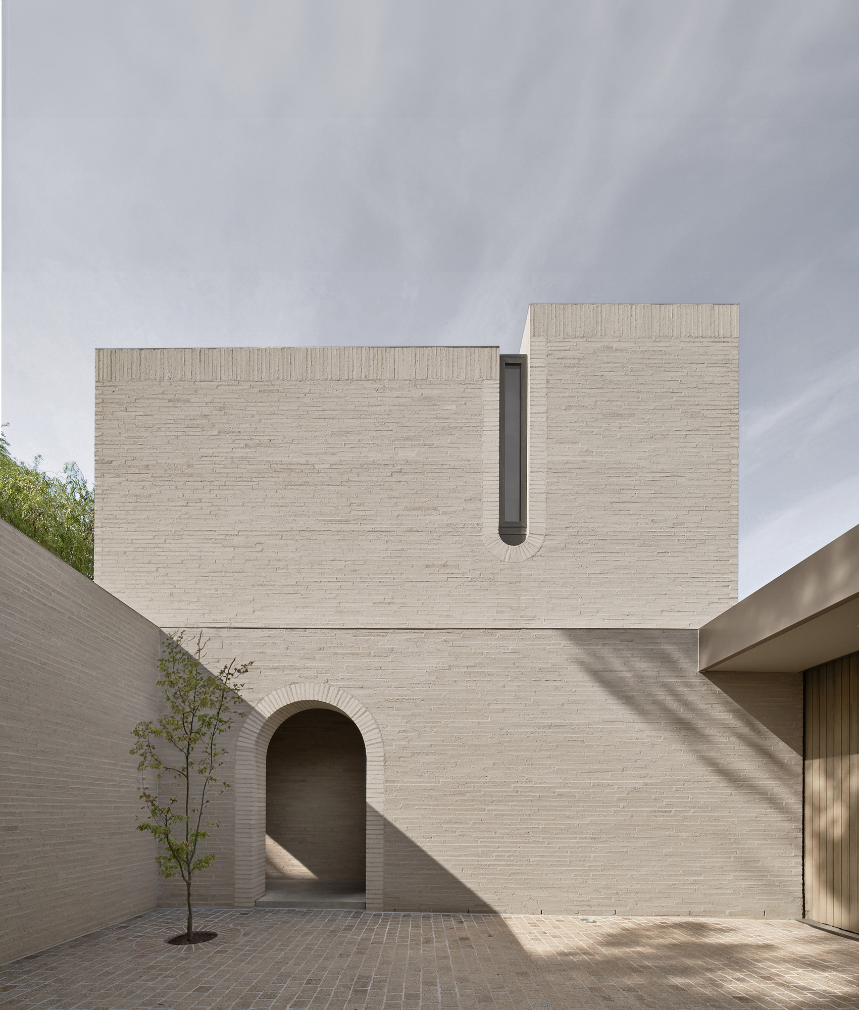 Casa Piva by B.E. Architecture, photographed by Peter Clarke — The full elevation of the white brick volume, slot window above and the arch set into the courtyard wall beneath.