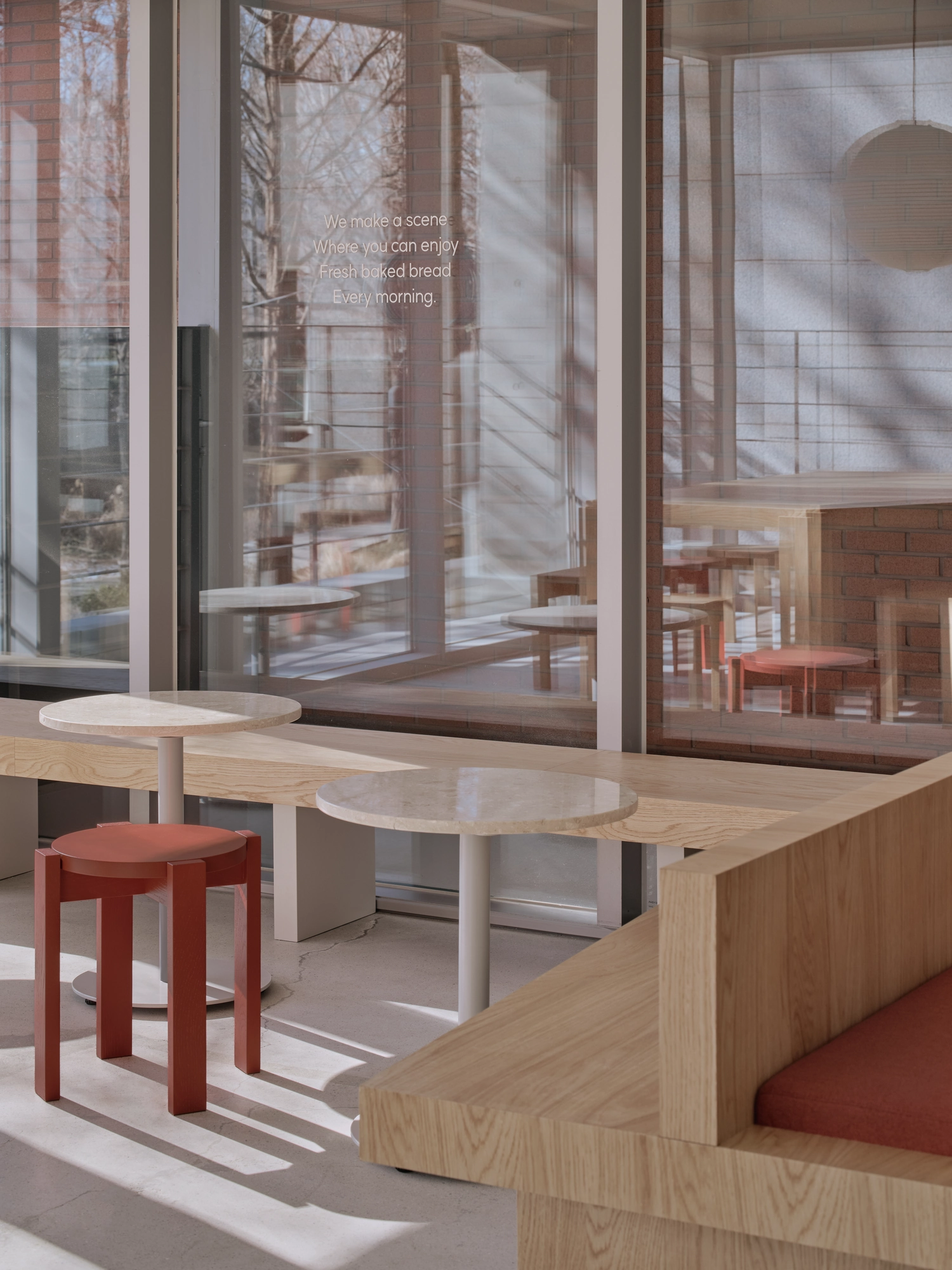 Bread&Walk by StudioFA, photographed by Dongkyu Kim — Round tables line a window-height shelf with stools pulled up, bench seating to the right and the park reflected in the glass.