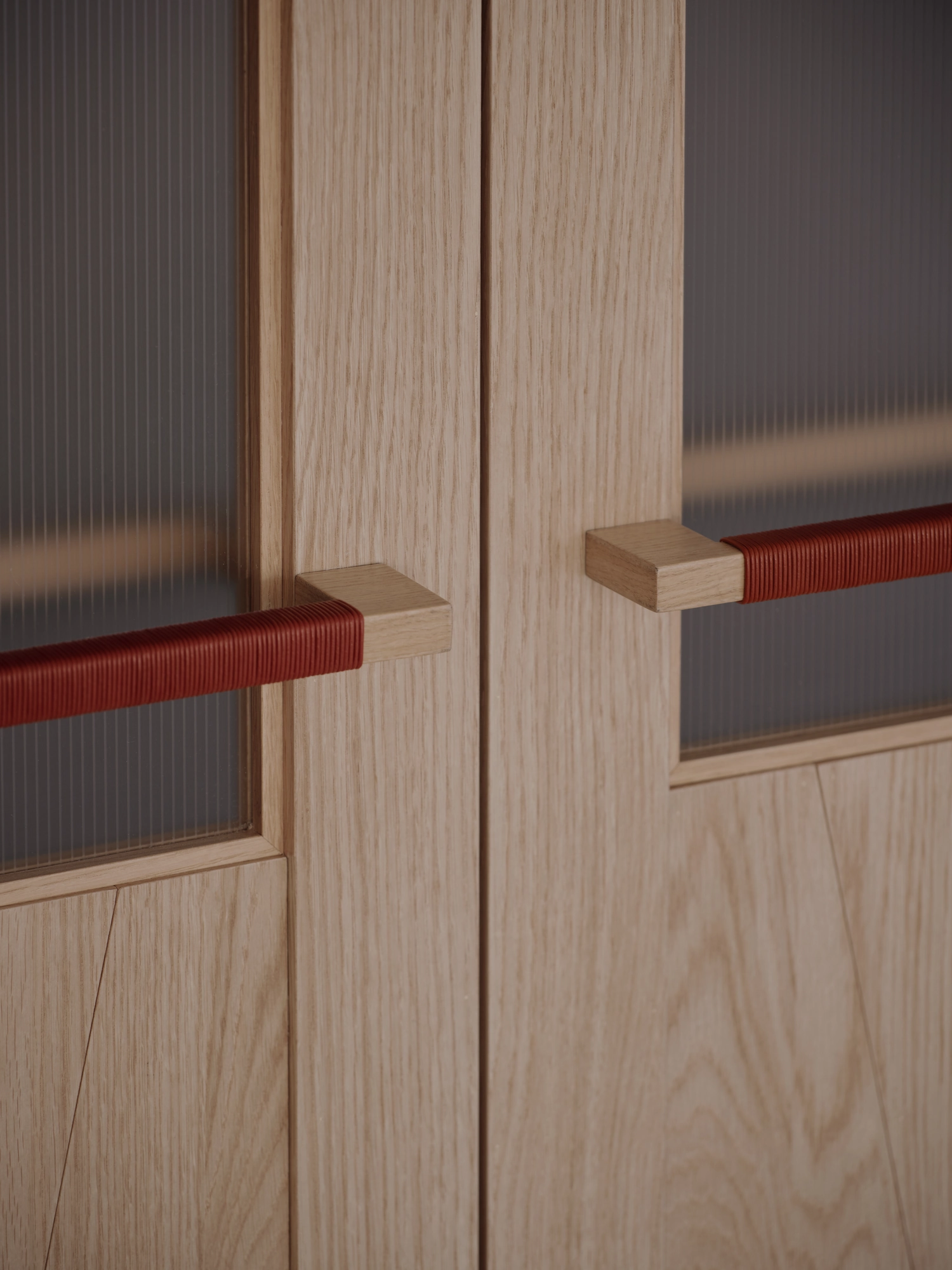Bread&Walk by StudioFA, photographed by Dongkyu Kim — A close view of two doors meeting, their long pull handles wrapped at the grip, set beside narrow glazed panels.