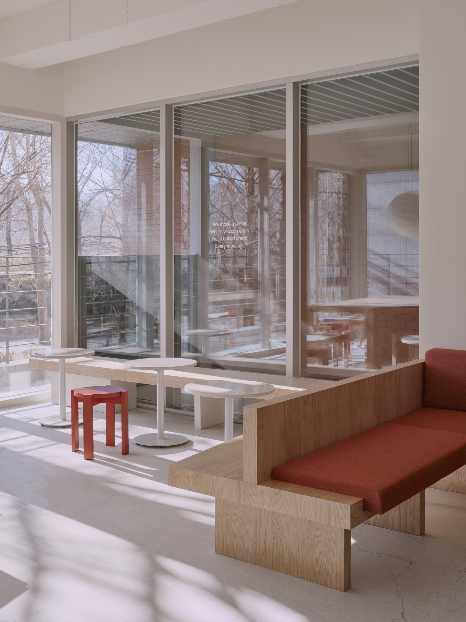 Bread&Walk by StudioFA, photographed by Dongkyu Kim — Bench seating wraps a corner beside tables set on a window shelf, a single stool nearby and the trail beyond the glass.