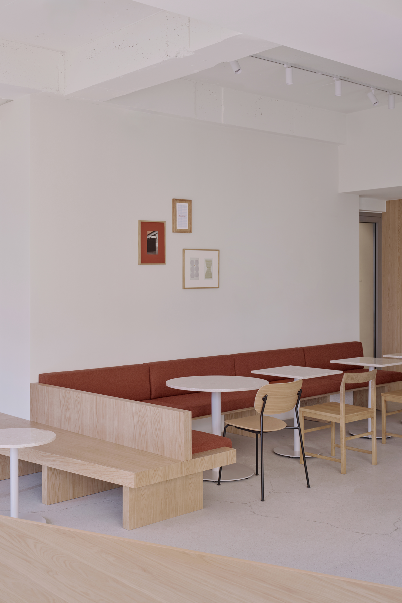 Bread&Walk by StudioFA, photographed by Dongkyu Kim — A run of bench seating sits below three framed pictures, with round tables, chairs and a low bench, track lights overhead.