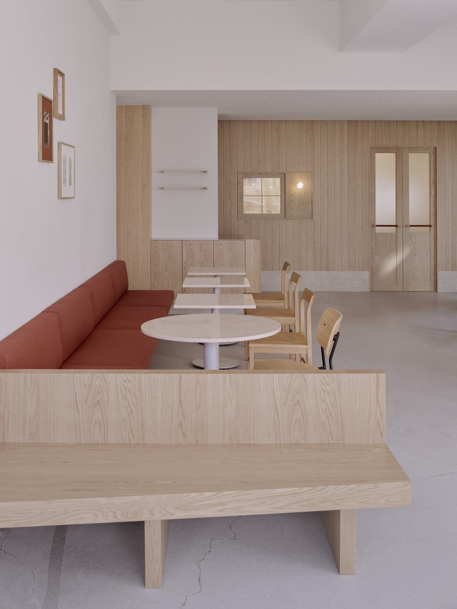 Bread&Walk by StudioFA, photographed by Dongkyu Kim — Bench seating runs beside round tables and chairs, a low backless bench set in front and framed pictures hung above.