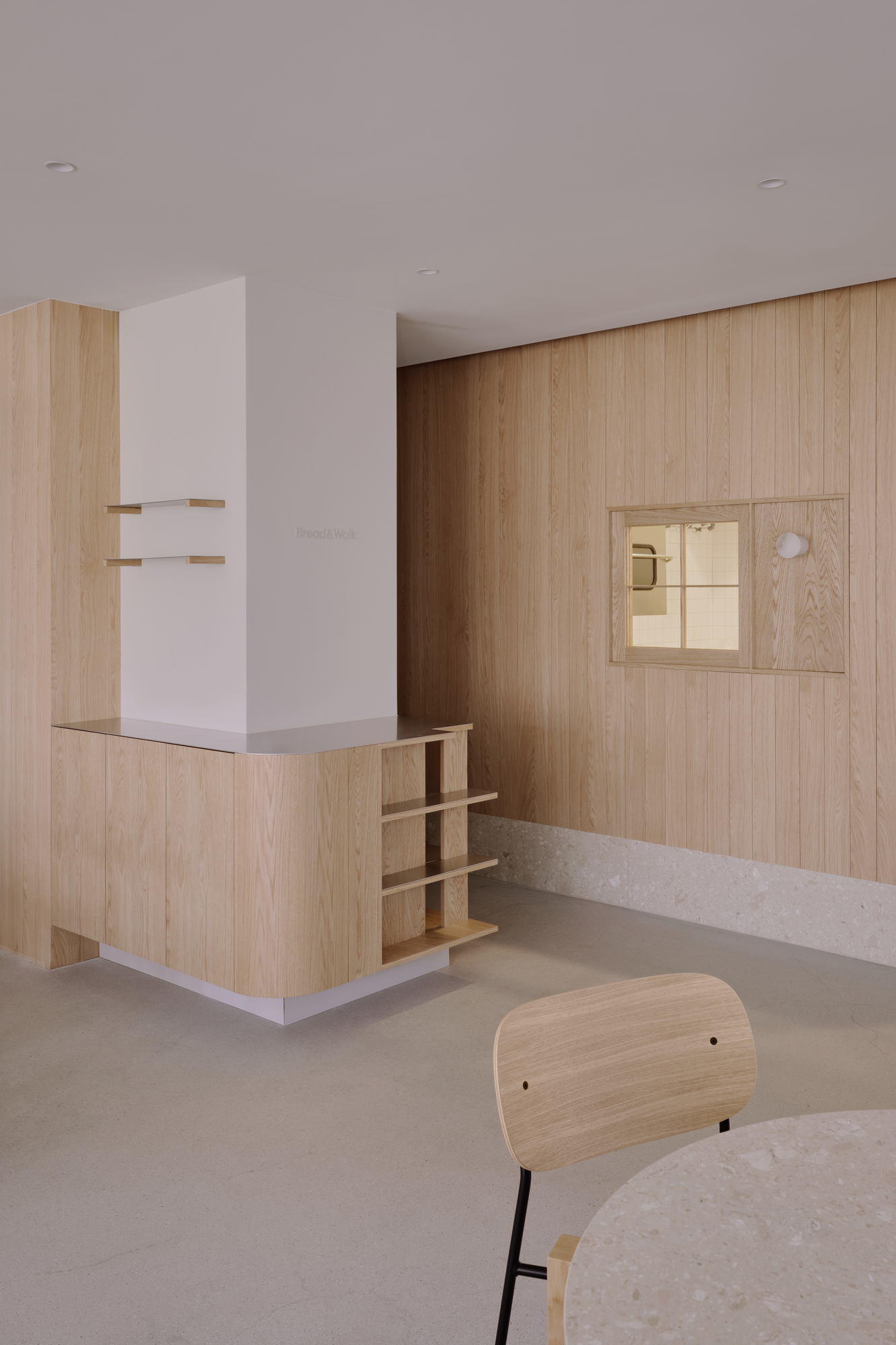 Bread&Walk by StudioFA, photographed by Dongkyu Kim — A counter of open shelving sits below the shop's name, a small interior window alongside, a chair in front.