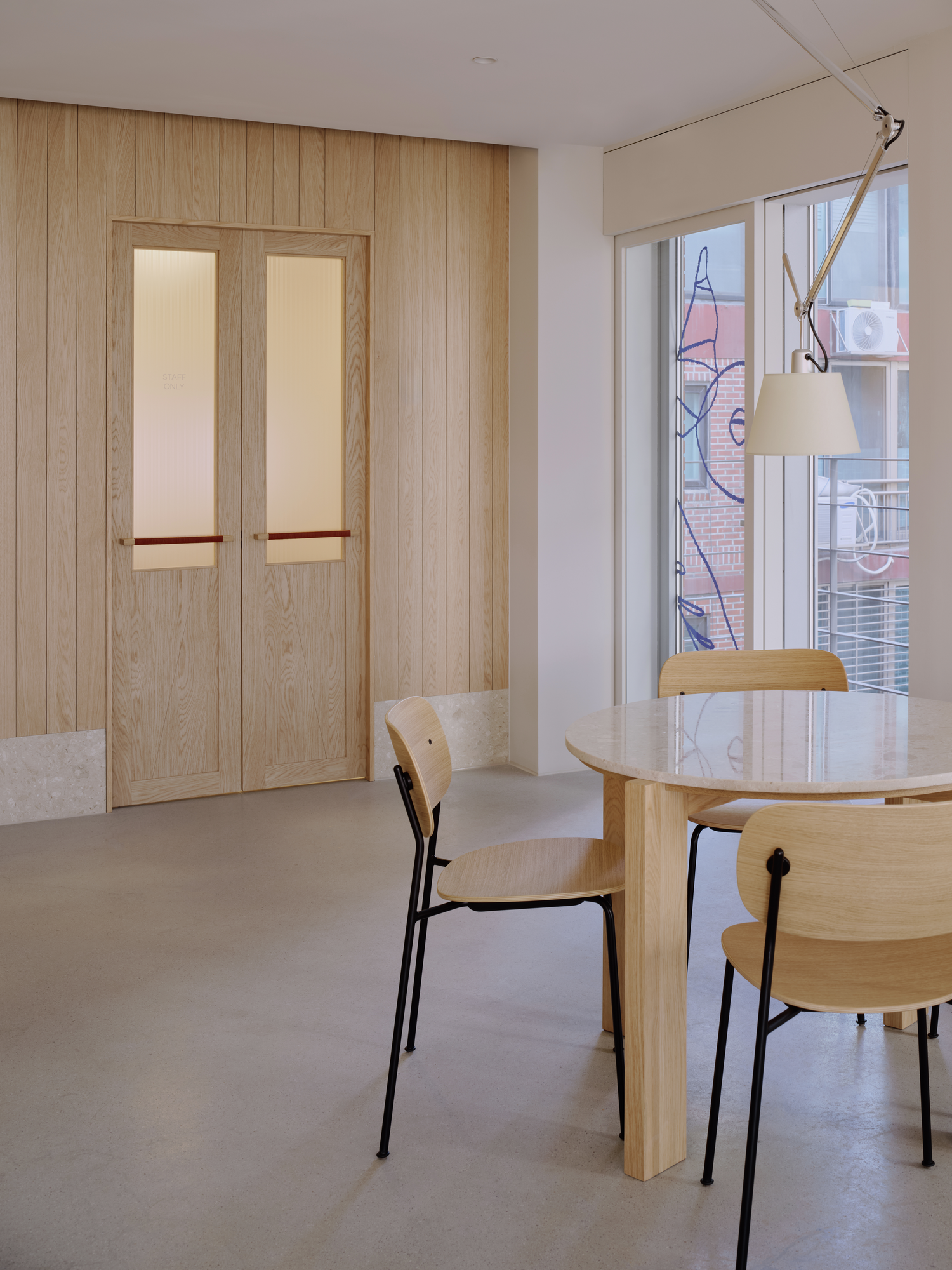 Bread&Walk by StudioFA, photographed by Dongkyu Kim — A pair of doors sits beside a round table and chairs, a task lamp angled from the ceiling toward the window.