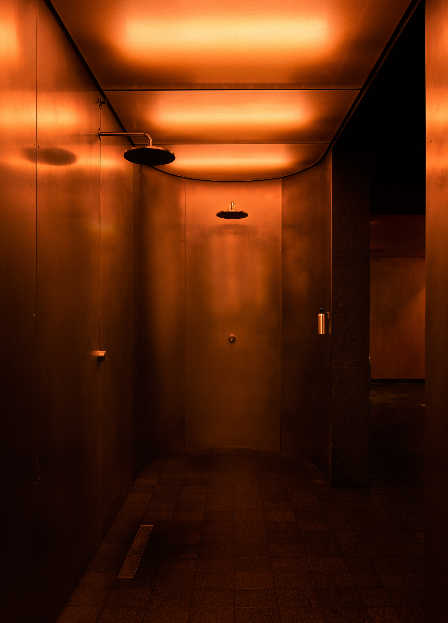 The Altar by MV-LLC — The collective showers, their brushed stainless steel walls refracting the indirect light above.