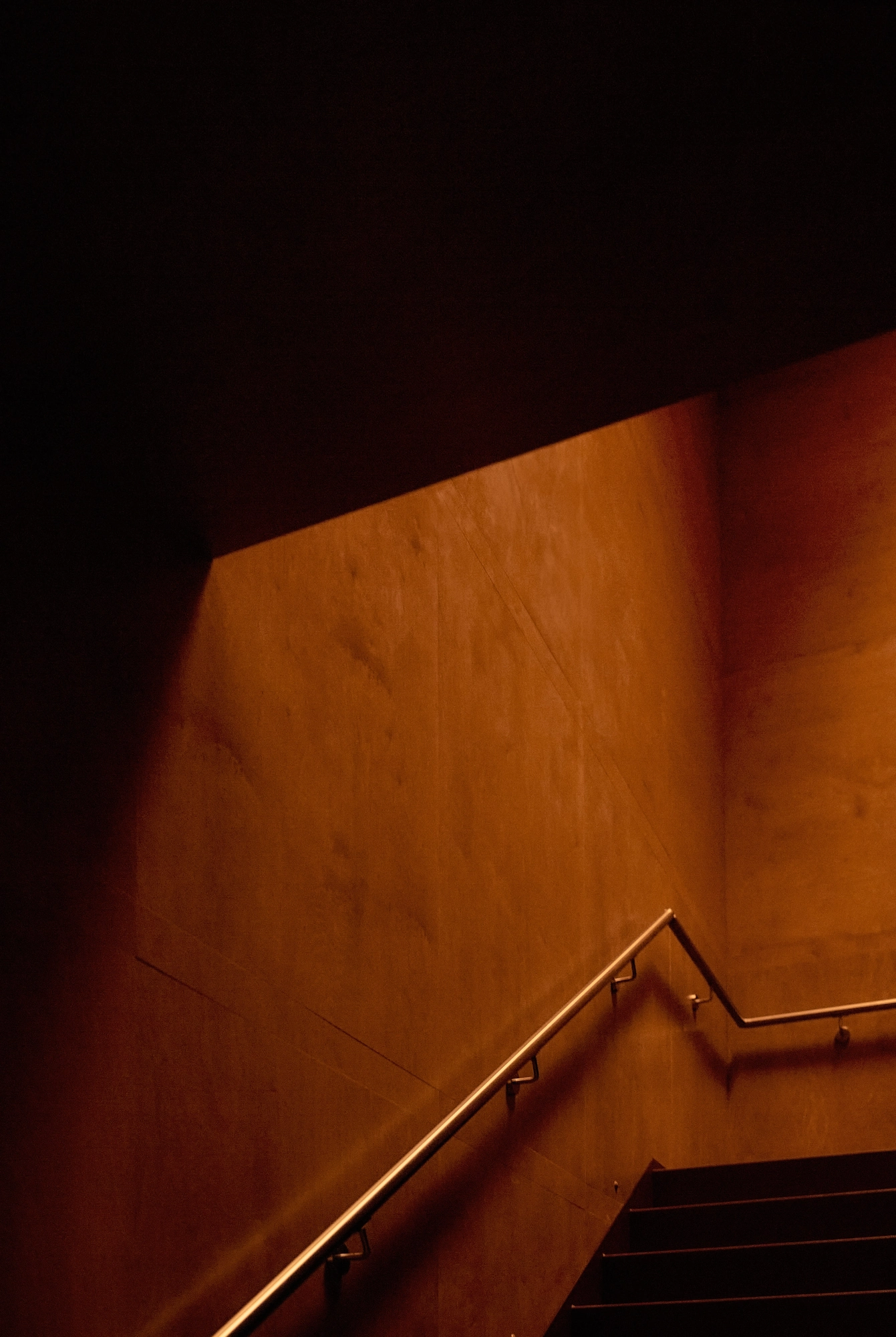 The Altar by MV-LLC — Calibrated seams on the wood-paneled stairwell wall, a solid handrail running down the descent.