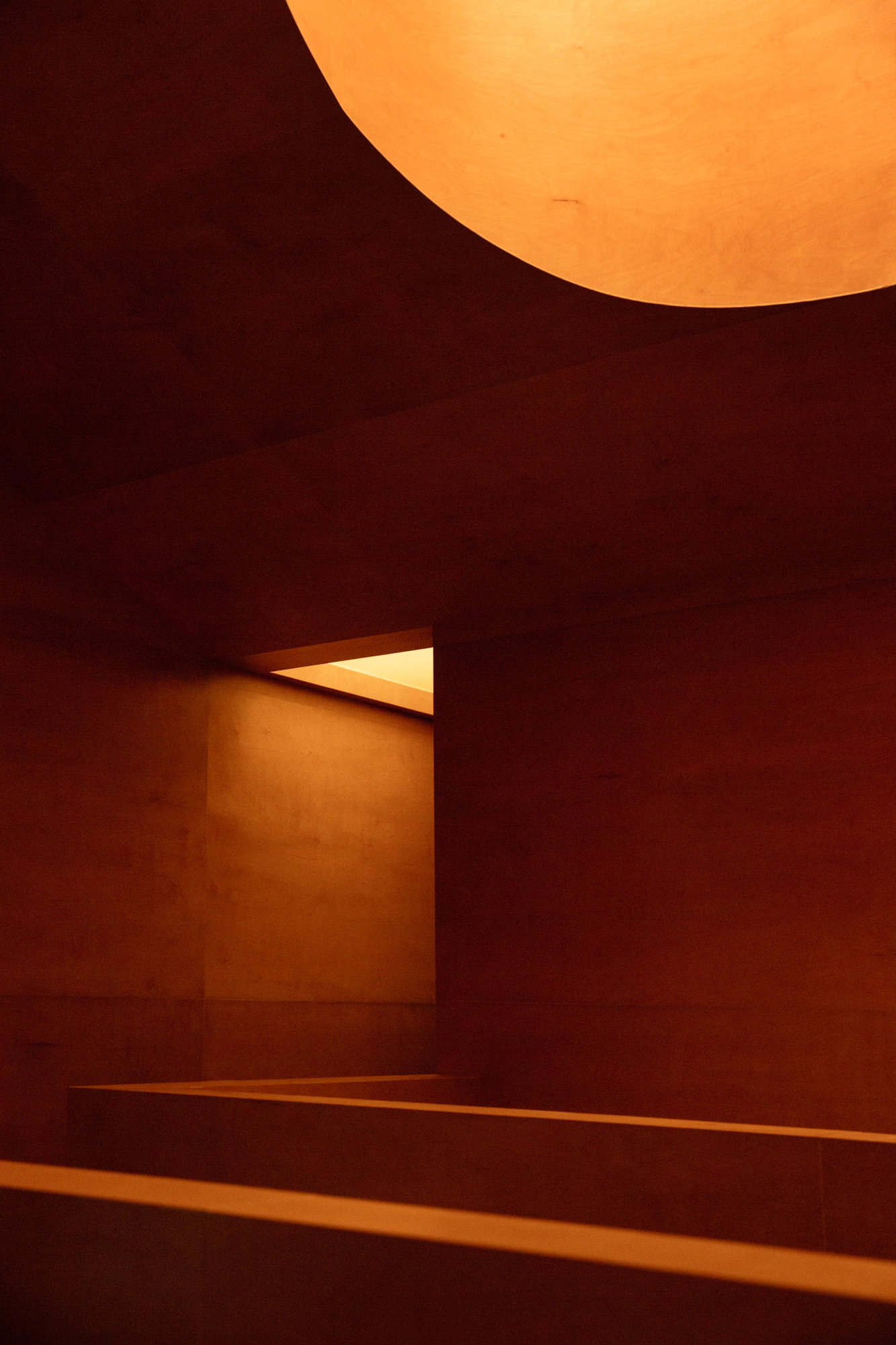 The Altar by MV-LLC — Stained plywood lines the stair rising toward the glowing oculus overhead.