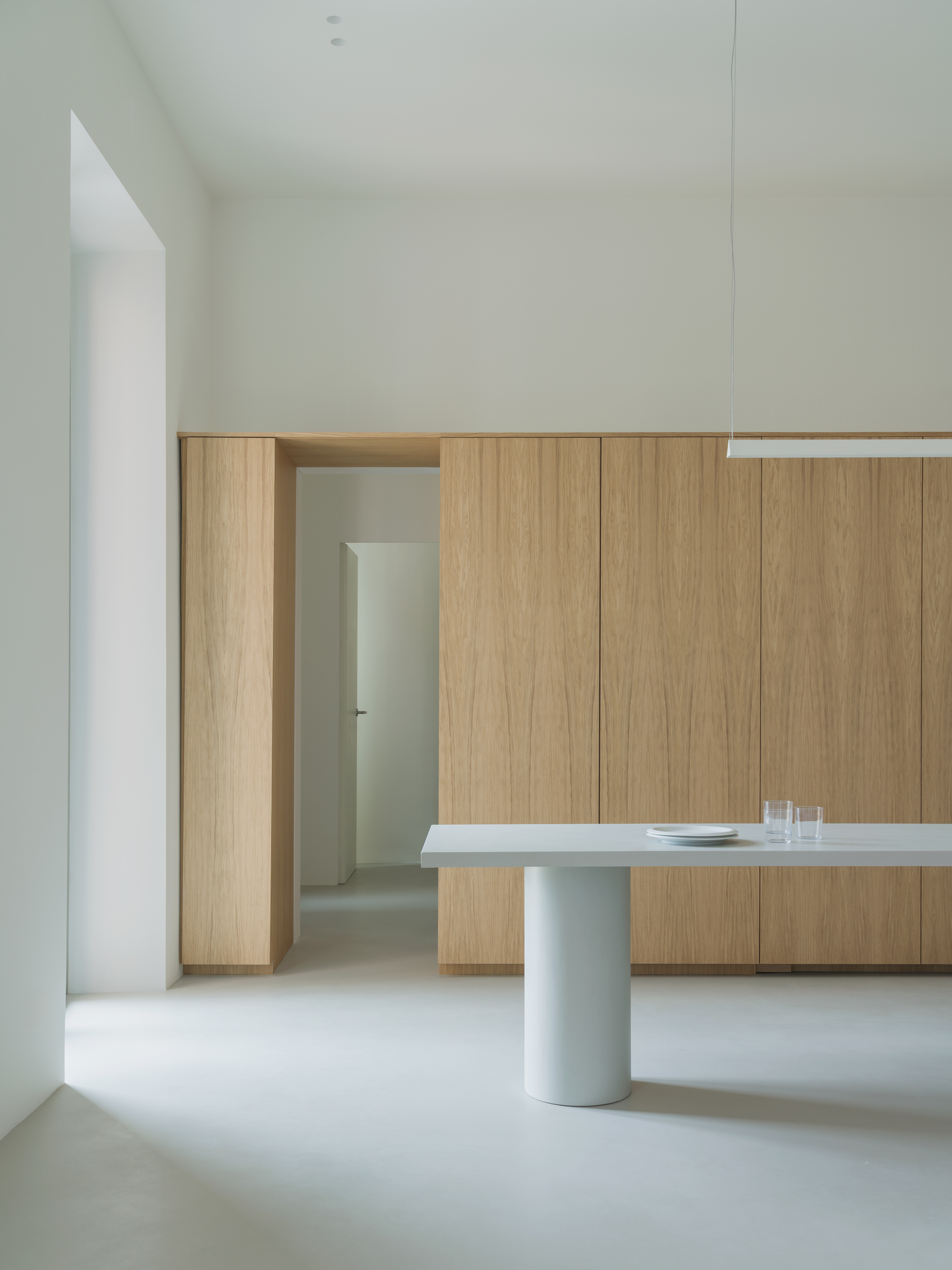 House with a White Column by SET Architects, photographed by Daniele Criscenzo — A doorway cut into the oak wall leads to a corridor, with the end of the table on its cylindrical leg in the foreground.