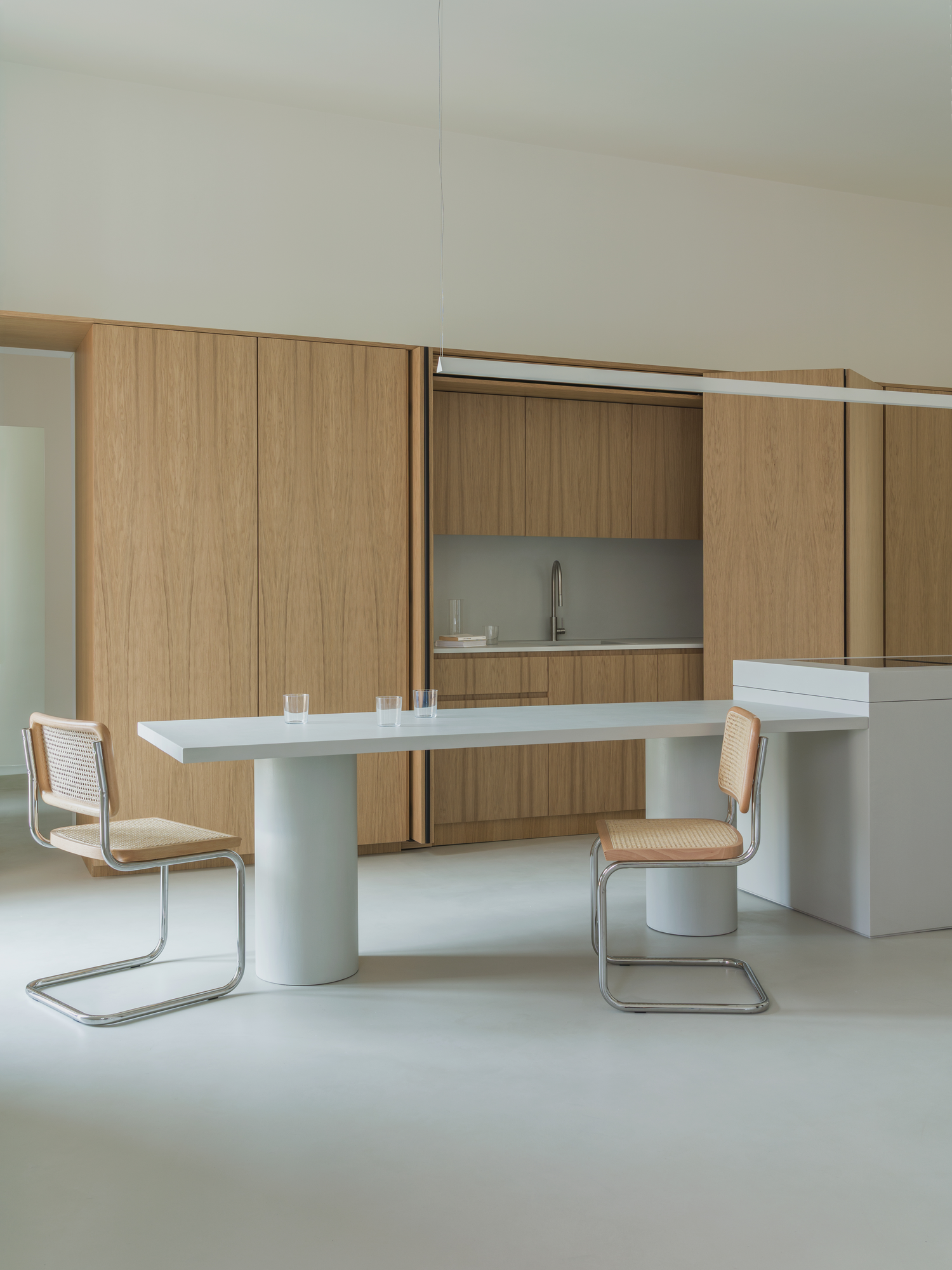 House with a White Column by SET Architects, photographed by Daniele Criscenzo — The kitchen opened at its centre to show a sink between oak doors, with the table, chairs and the edge of the island in front.