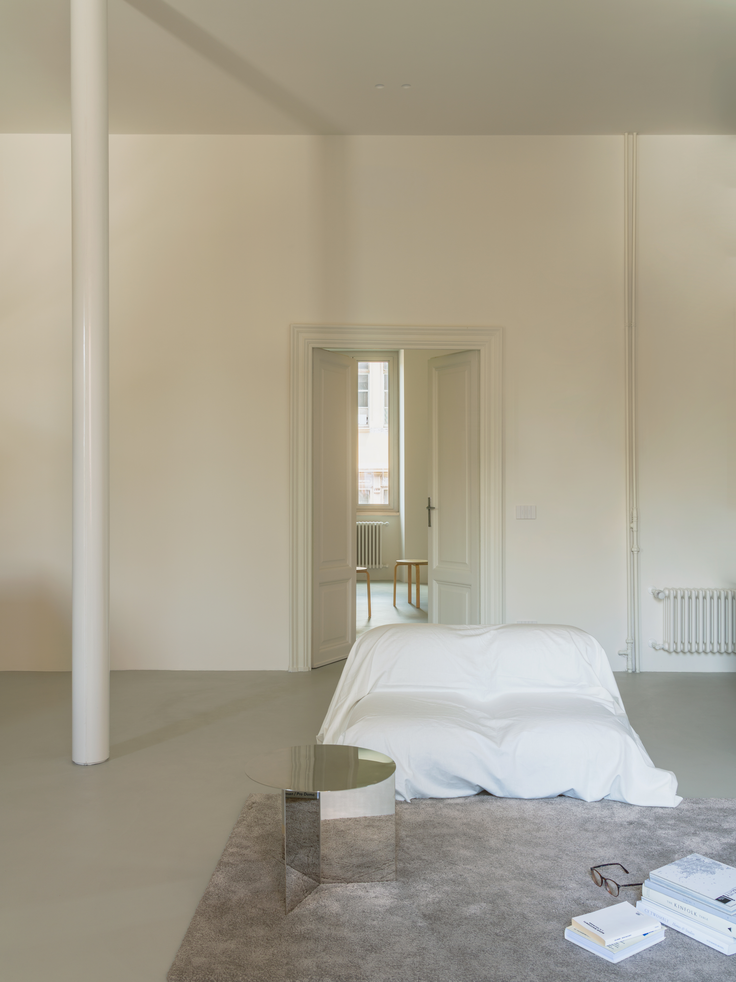 House with a White Column by SET Architects, photographed by Daniele Criscenzo — Open double doors lead to a room with a window, past a draped seat and the white column on the left.