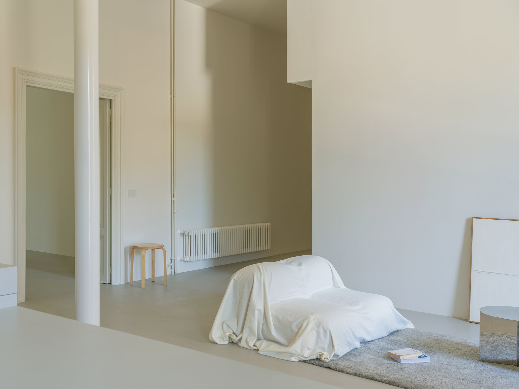 House with a White Column by SET Architects, photographed by Daniele Criscenzo — The white column in the foreground, with a doorway, a radiator and a seat draped in a sheet beyond it.