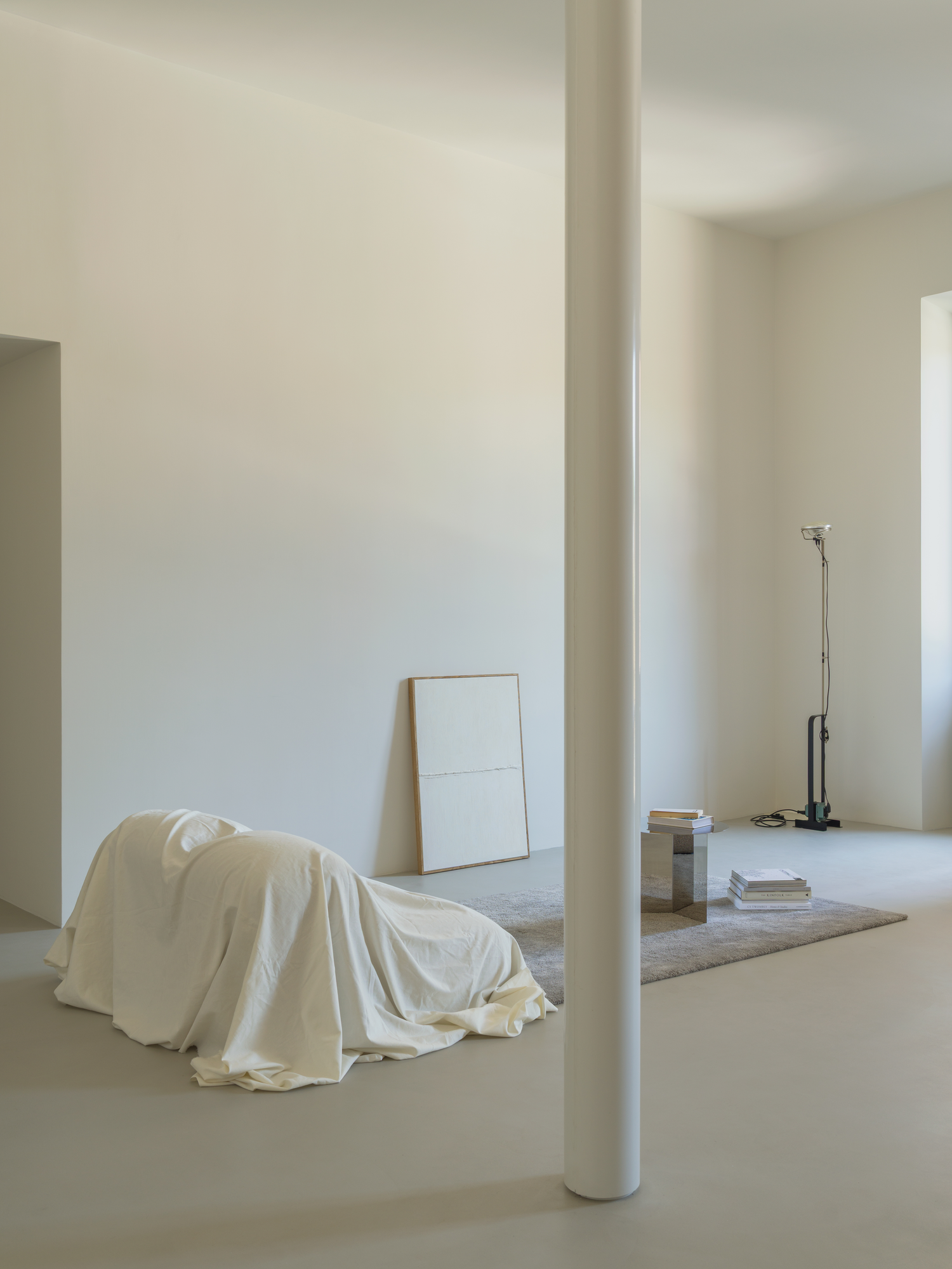 House with a White Column by SET Architects, photographed by Daniele Criscenzo — The white column stands in the middle of the view, with a draped seat, a frame leaning against the wall and a floor lamp in the far corner.