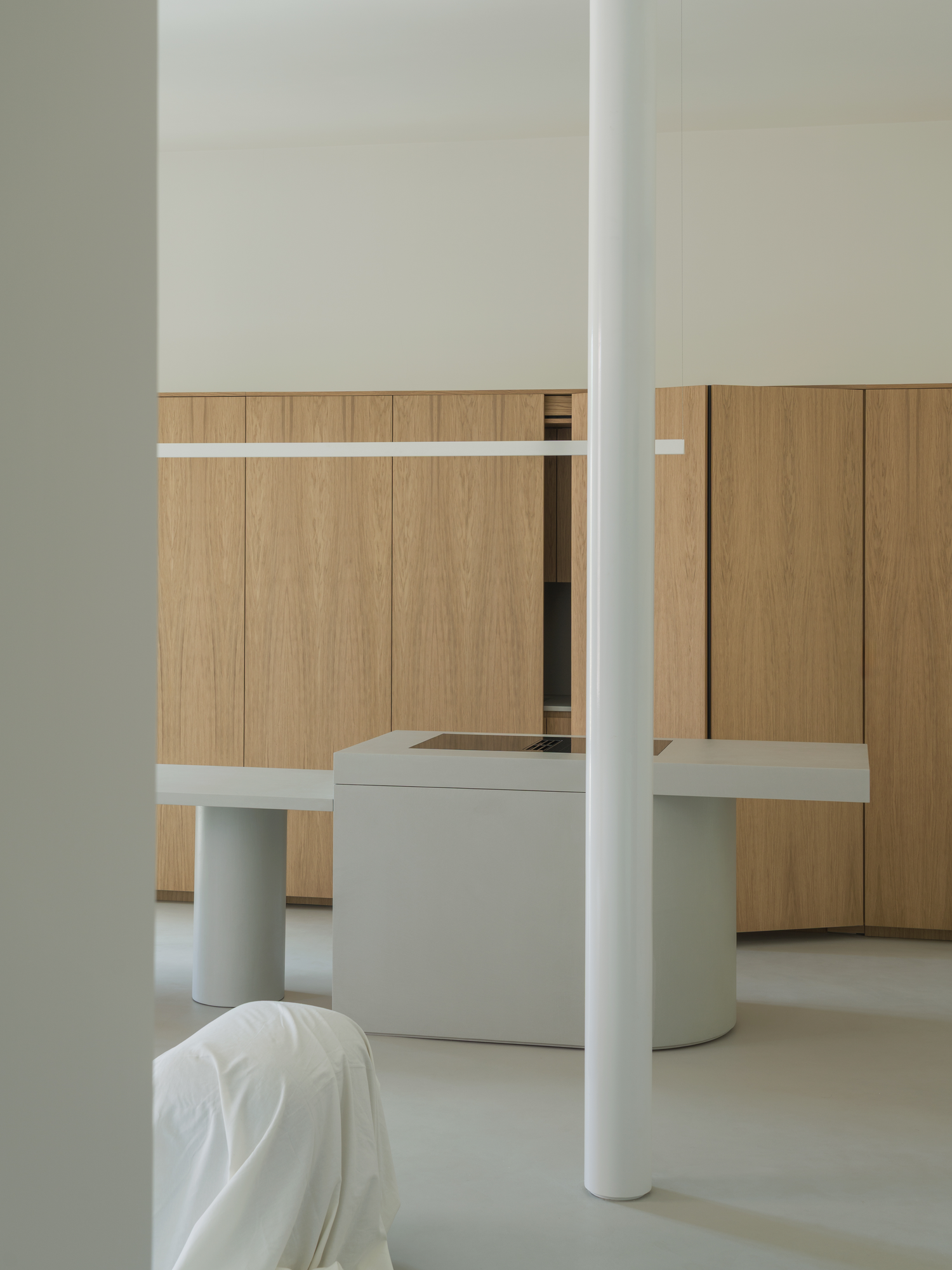 House with a White Column by SET Architects, photographed by Daniele Criscenzo — The white column stands before the microcement island and table, with the oak wall behind and one of its doors partly open.