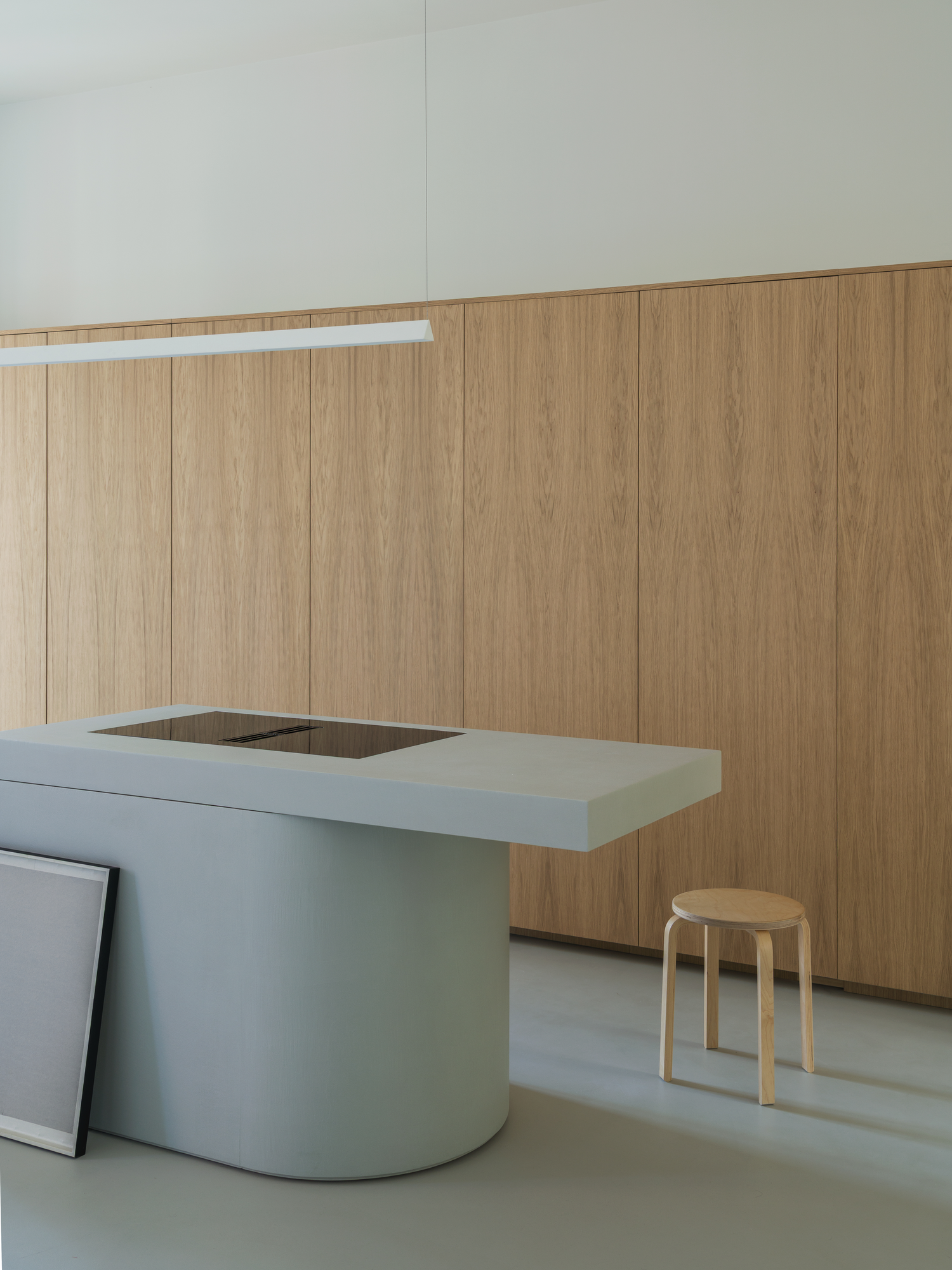 House with a White Column by SET Architects, photographed by Daniele Criscenzo — The rounded end of the microcement island with its cooktop, set against a continuous run of oak doors, a stool beside it.