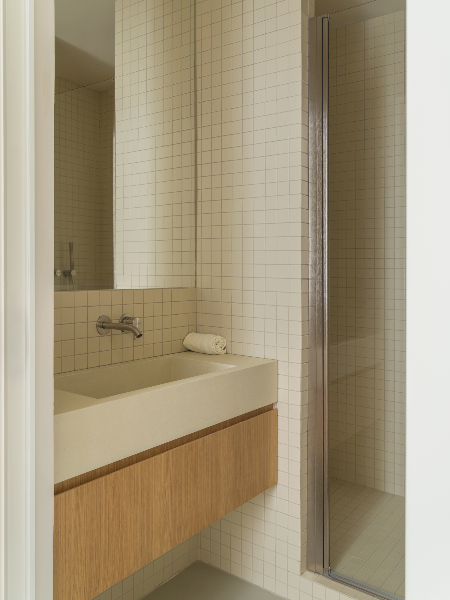 House with a White Column by SET Architects, photographed by Daniele Criscenzo — A bathroom with a basin set over a drawer, a mirror above it and a shower behind a door to the right.