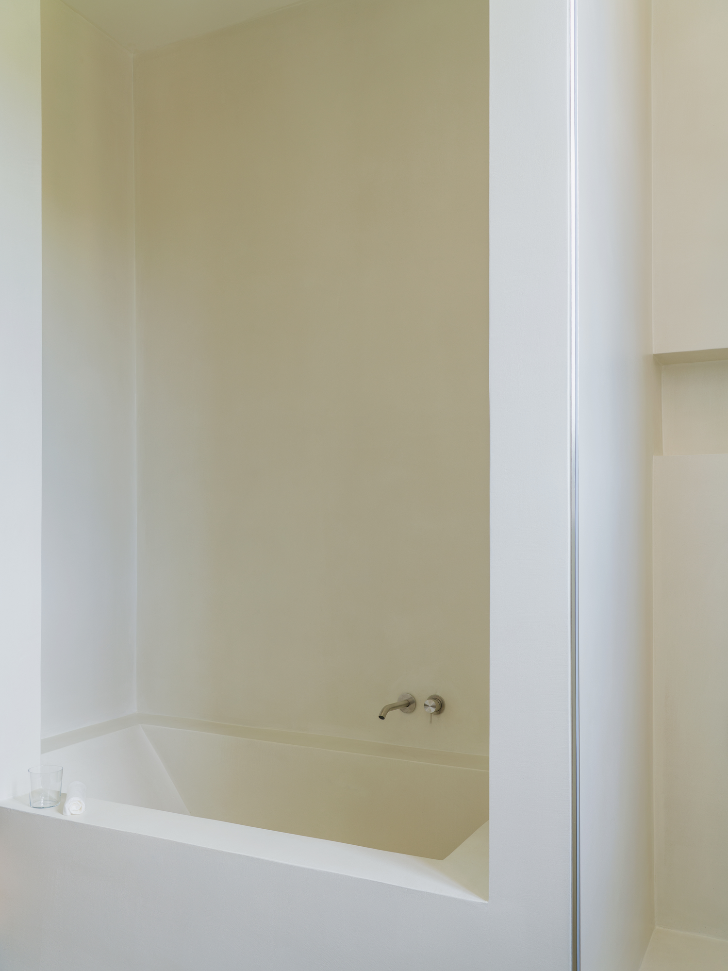House with a White Column by SET Architects, photographed by Daniele Criscenzo — A bath set into a recess in a white wall, with a wall-mounted tap above its rim.
