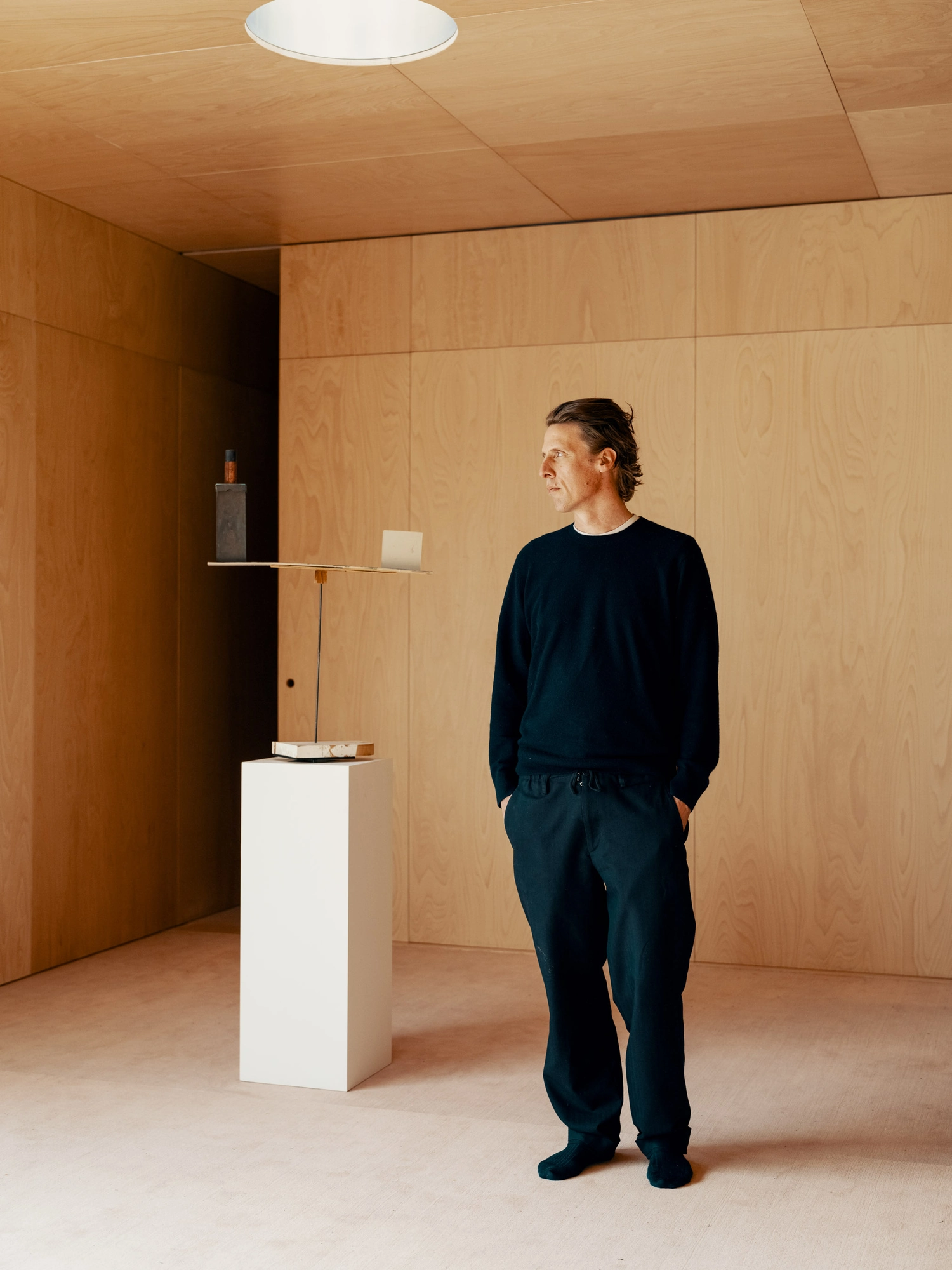 Atelier Van de Velde by OFFICE Kersten Geers David Van Severen, photographed by Senne & Eefje — Rinus Van de Velde standing in a wood-panelled room beside a white plinth.
